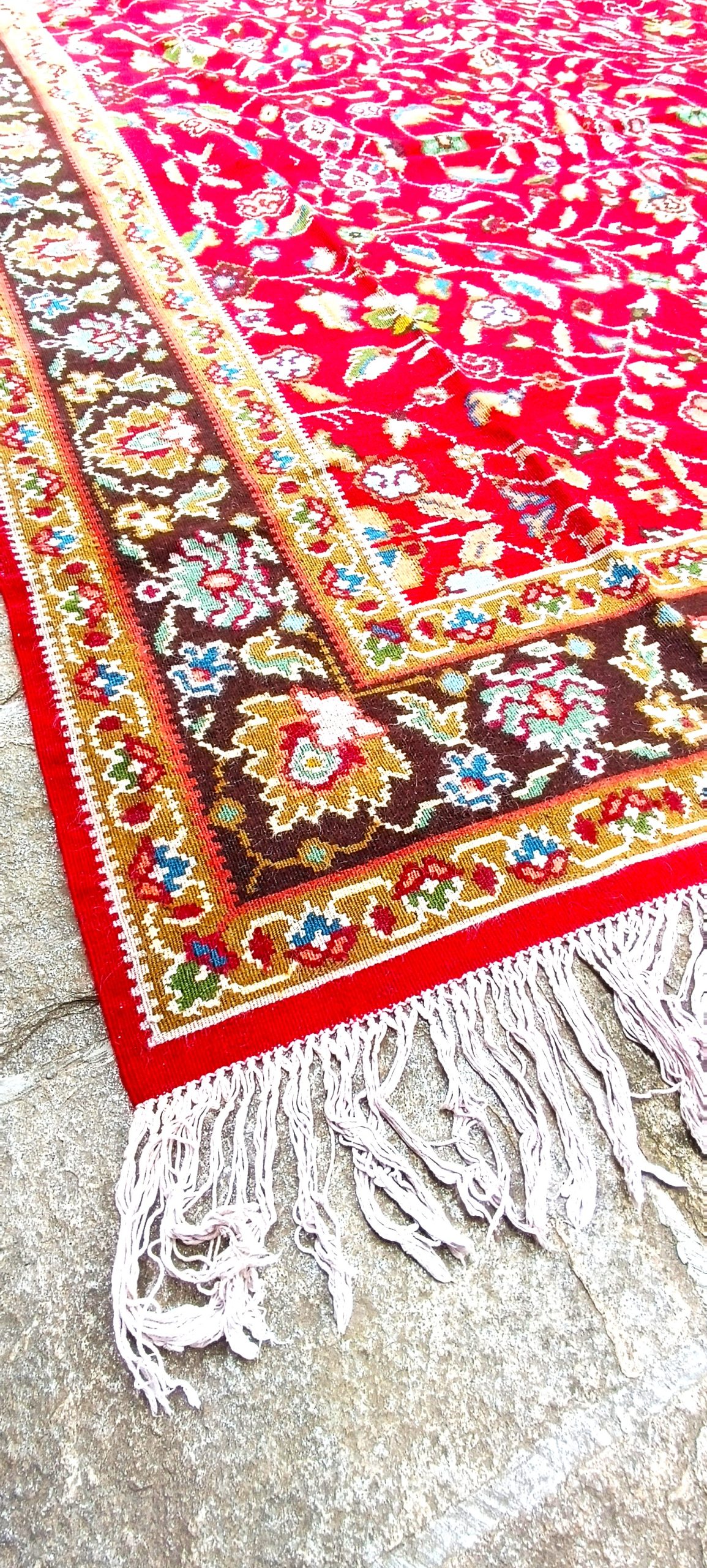 Детайл от котленски килим с тъмнокафяв флорален бордюр, червено поле и светли ресни.