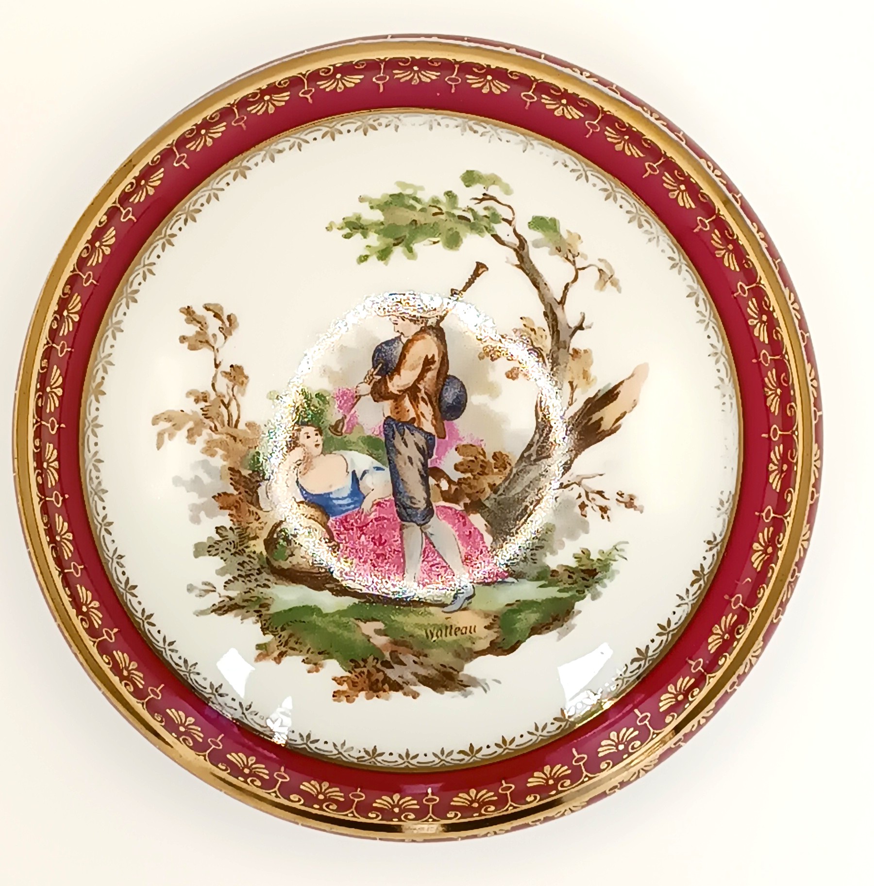 Top view of a Limoges France porcelain box lid with a Watteau-style scene and red gilt border