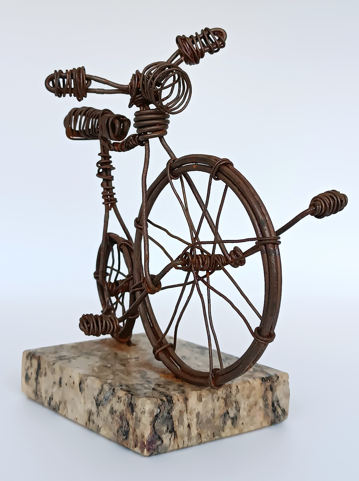 Side view of handmade Penny-farthing wire bicycle sculpture on stone base
