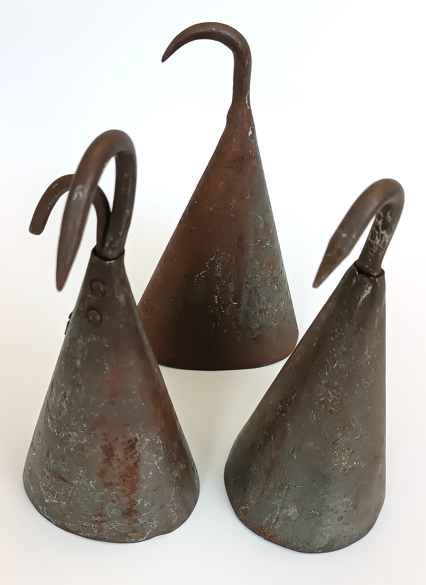 Three vintage forged iron butcher pig scraper bells with curved hooks and aged patina