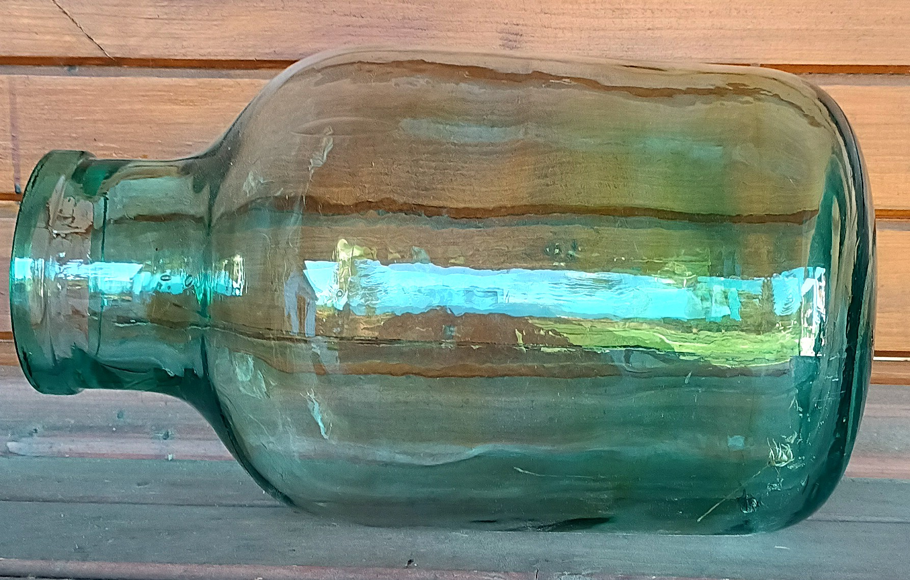 Side view of vintage green glass 8-litre demijohn with wide mouth and thick blue-green glass