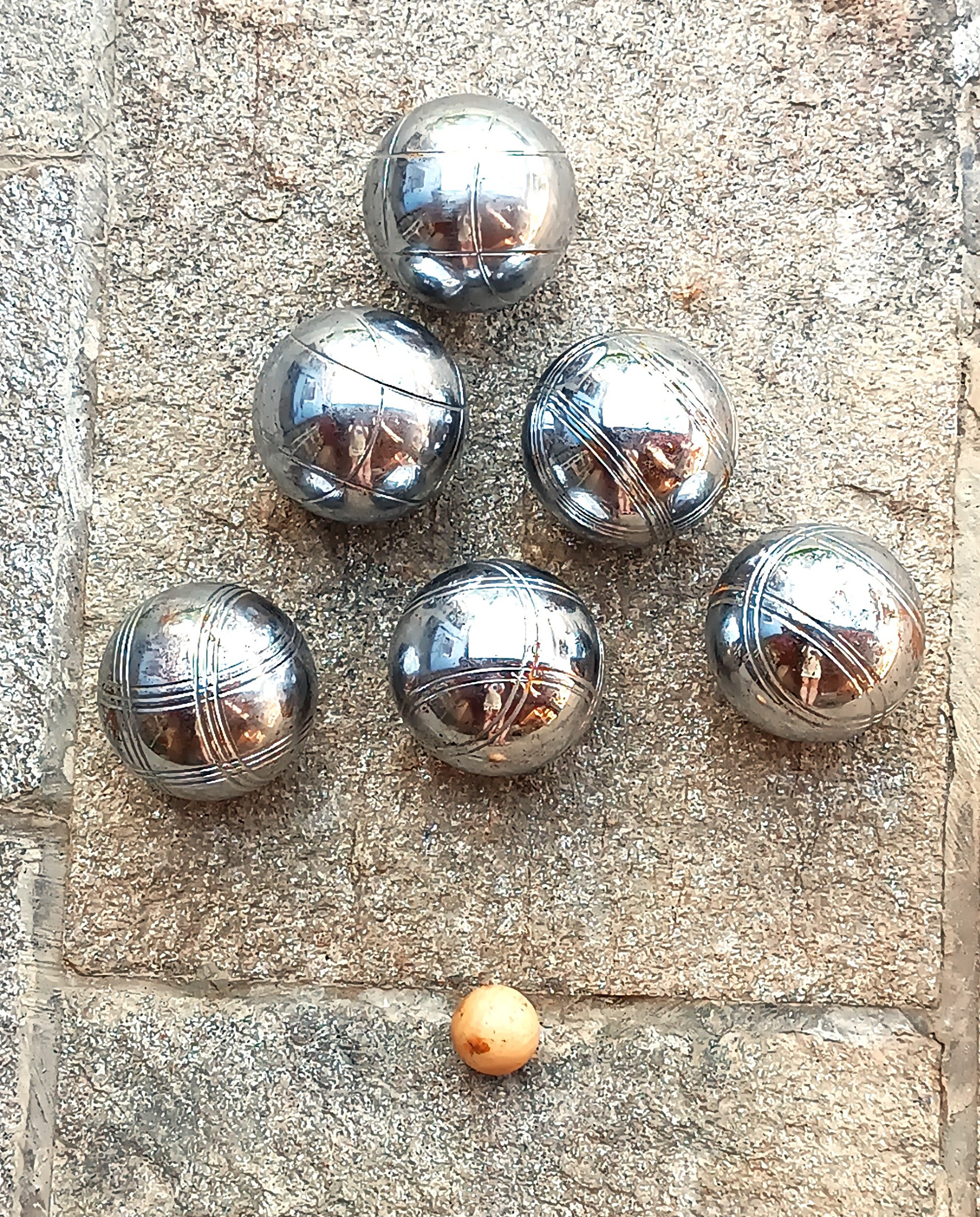 Vintage pétanque set with 6 solid metal boules and a wooden jack arranged on stone paving
