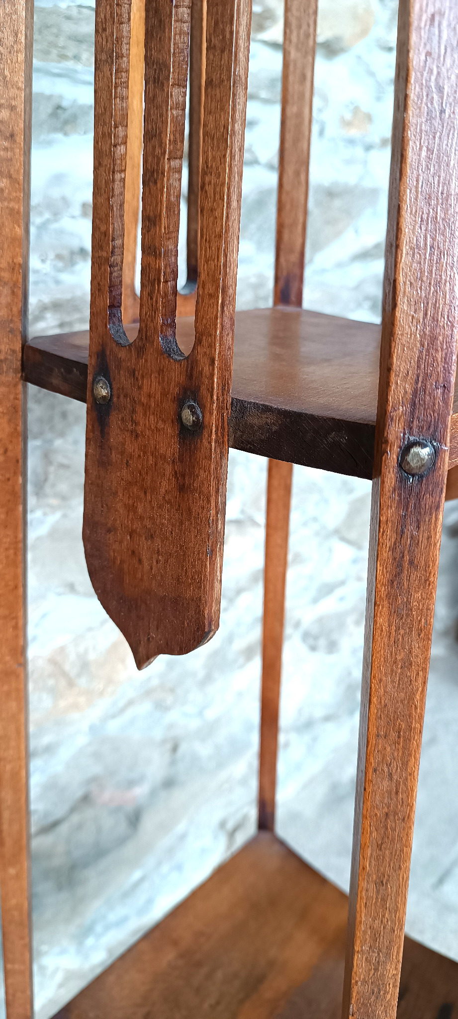 Close-up of an antique Balkan steamed beech plant stand showing brass rivets, decorative vertical cutouts and aged wood