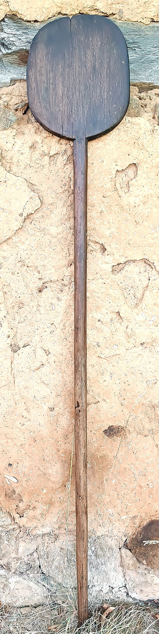 Full-length view of an antique Balkan wooden bread peel with long handle, dark worn paddle and one-piece solid wood construction