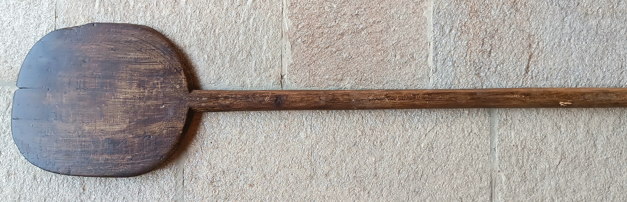 Horizontal view of an antique Balkan wooden bread peel with a long solid-wood handle, dark worn paddle and one-piece construction