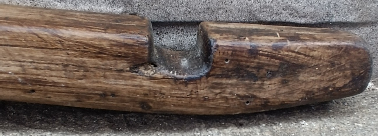 Close-up of an antique Bulgarian wooden shoulder yoke from Central Bulgaria showing the carved end notch, rounded end, natural patina and old crack