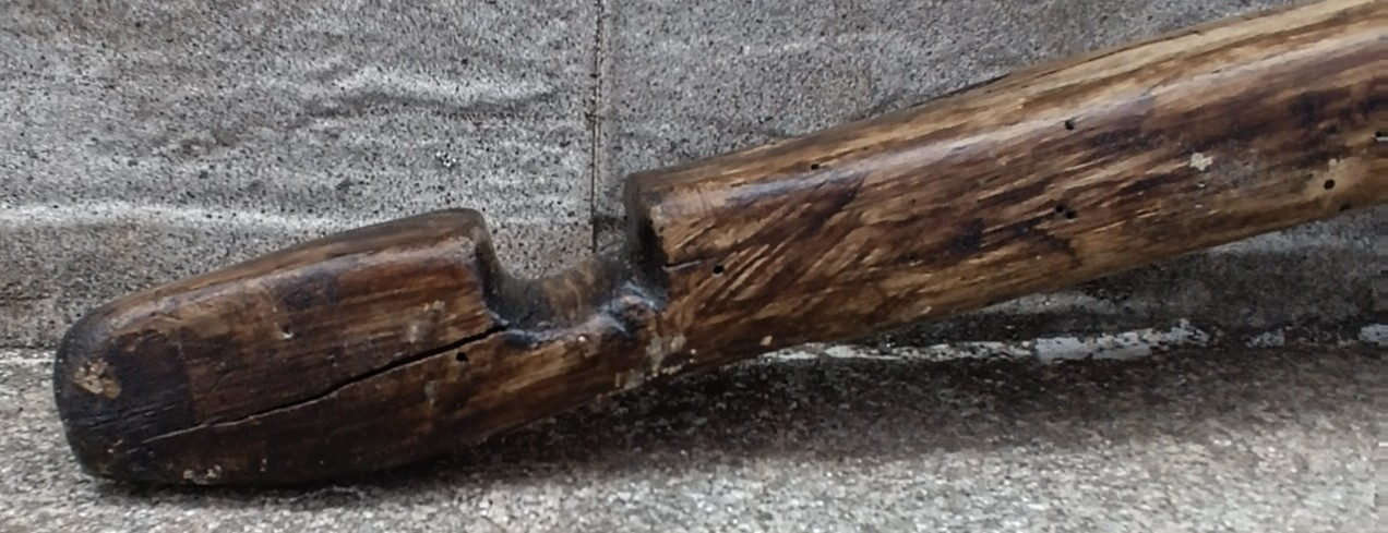 Close-up of an antique Bulgarian wooden shoulder yoke showing the rounded end, deep carved notch, old crack and naturally aged wood surface