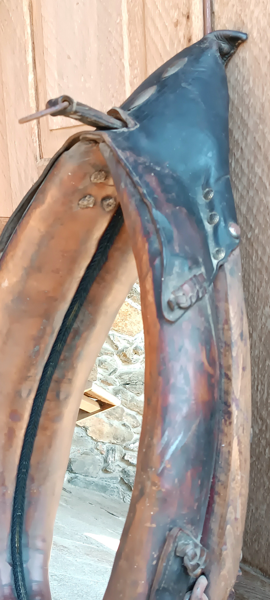 Close-up of the upper section of an antique horse collar mirror showing original leather, metal studs, straps and aged patina