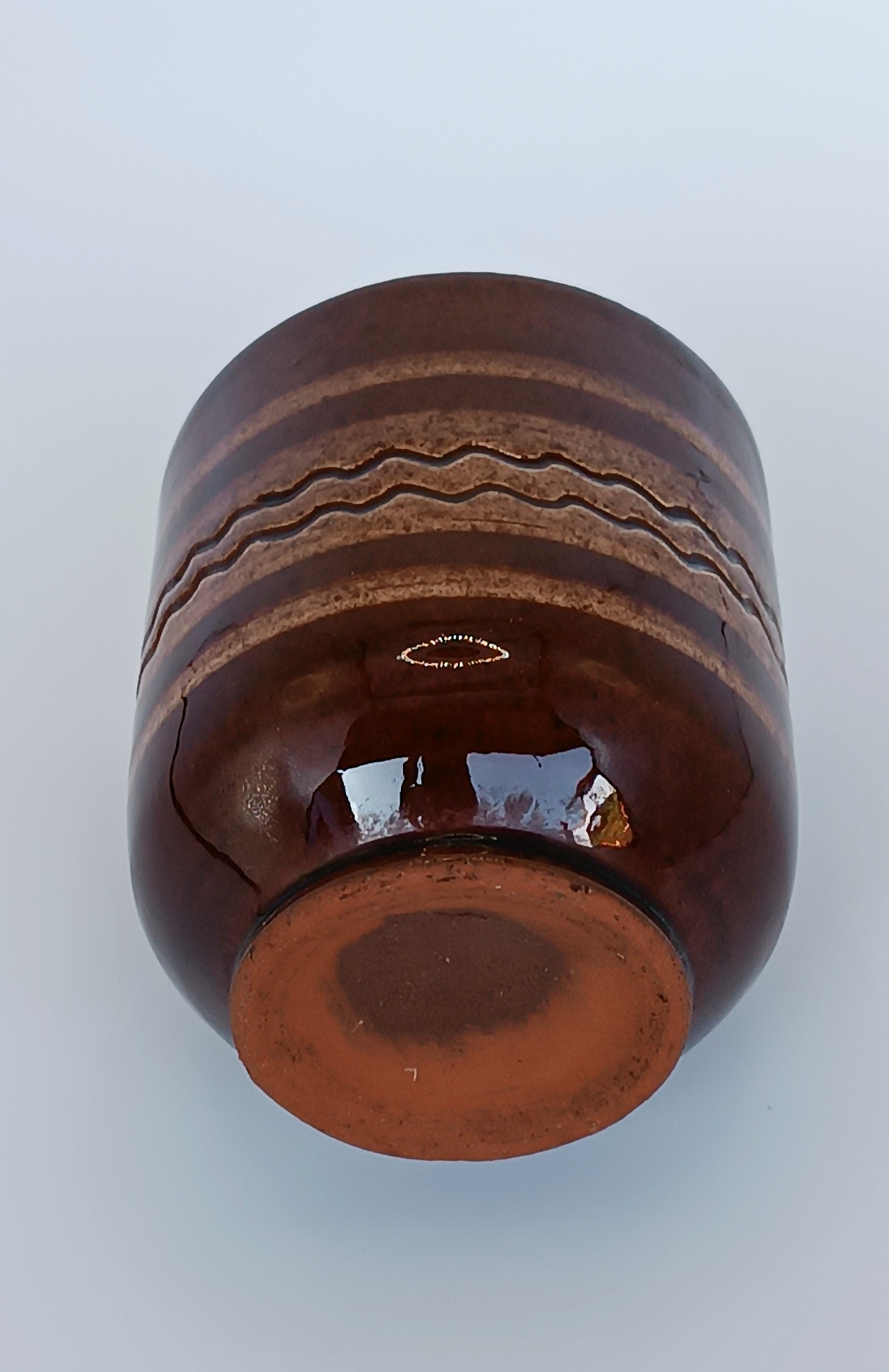 Underside of a vintage Balkan ceramic cup showing the unglazed terracotta base, glossy brown glaze and wavy folk decoration