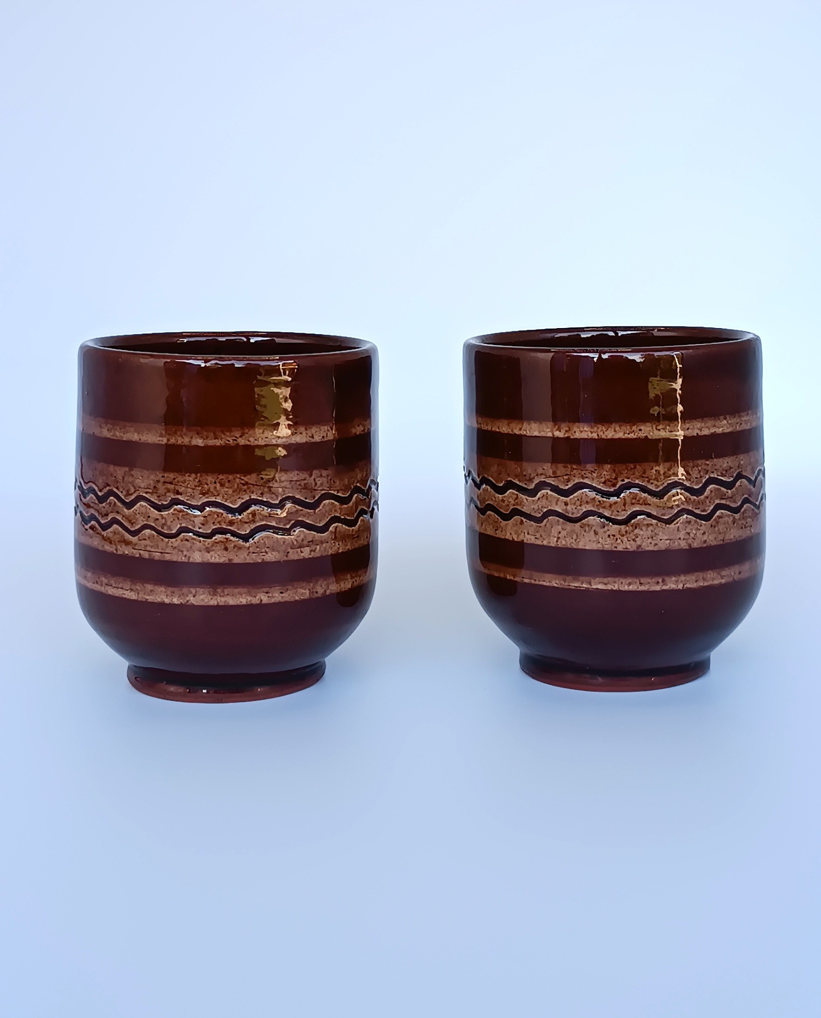 Two vintage Balkan ceramic cups with glossy brown glaze, horizontal bands and traditional wavy folk decoration