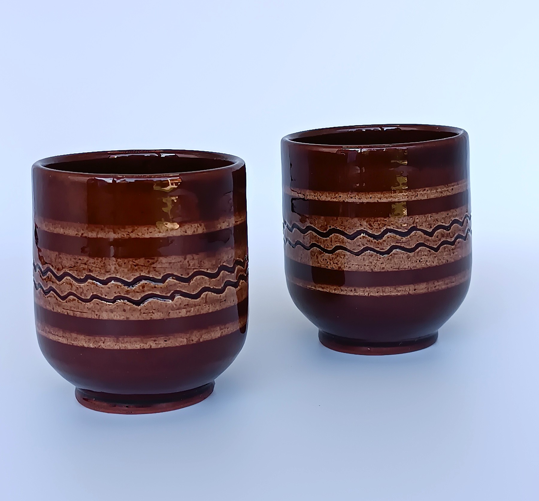 Pair of vintage Balkan ceramic cups with glossy brown glaze, horizontal bands and traditional wavy folk decoration