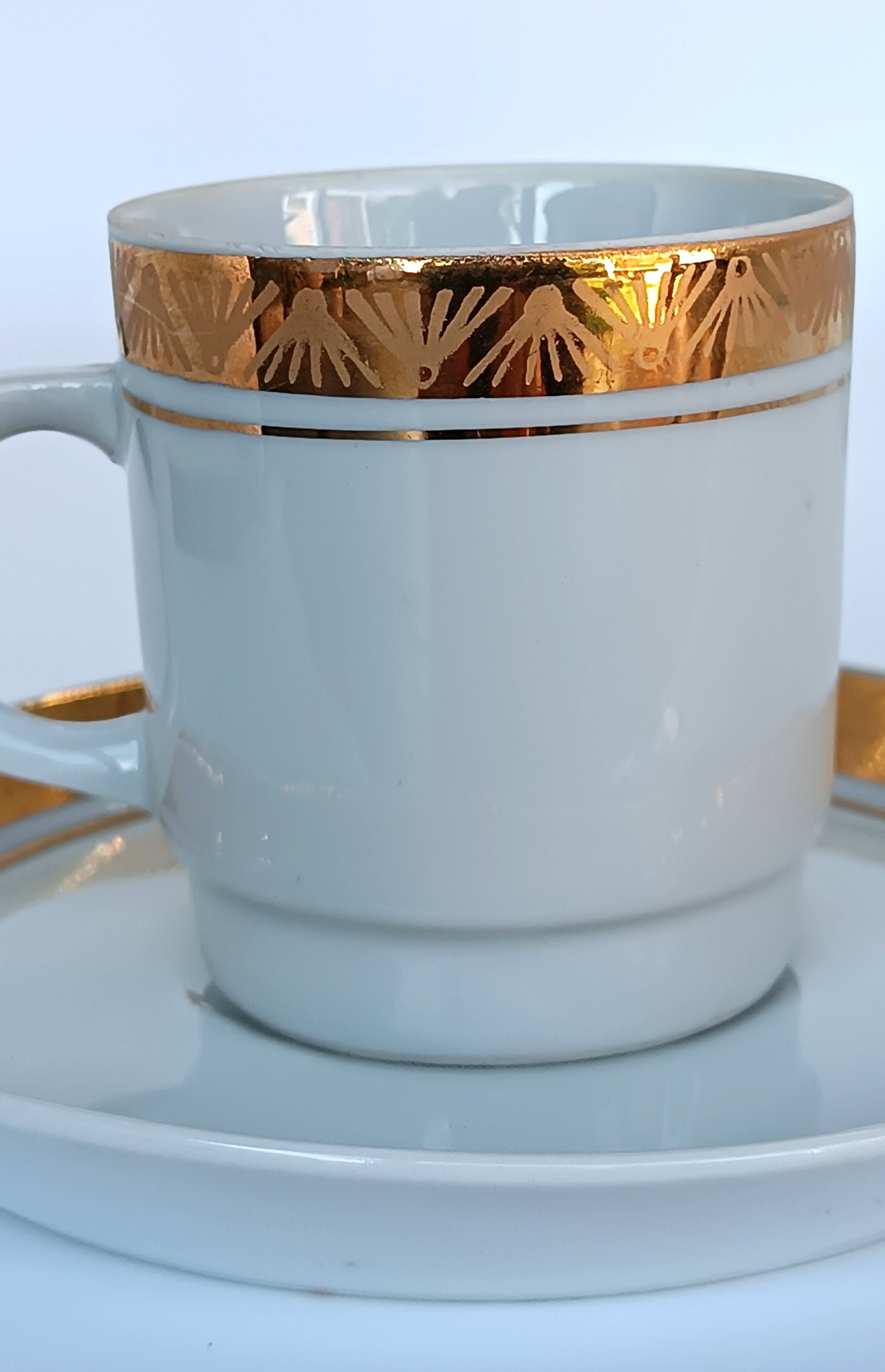 Close-up of a vintage Bulgarian porcelain coffee cup with matching saucer, wide gold geometric border and fine gold line decoration