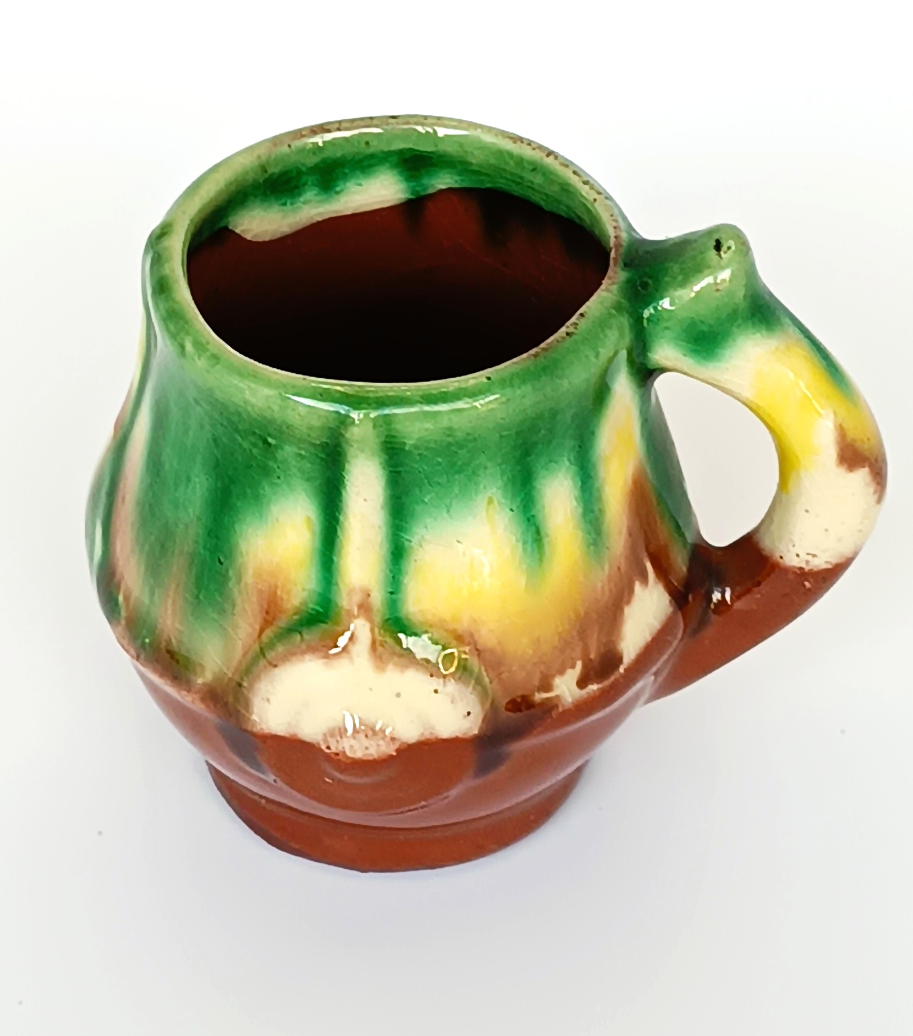 Top view of a vintage Bulgarian Troyan-style ceramic rakia cup with green, yellow, cream and brown glaze and curved handle