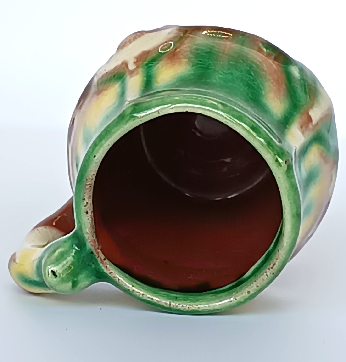 Underside of a vintage Bulgarian Troyan-style ceramic rakia cup showing the reddish earthenware base, green glaze and unmarked bottom