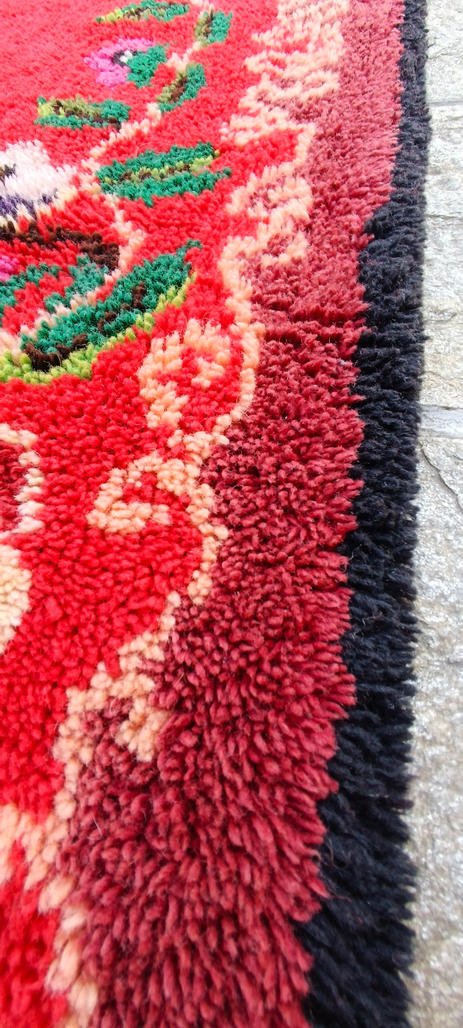 Close-up of a vintage Bulgarian handwoven wool kitenik showing dense floral pile, burgundy border and black outer edging