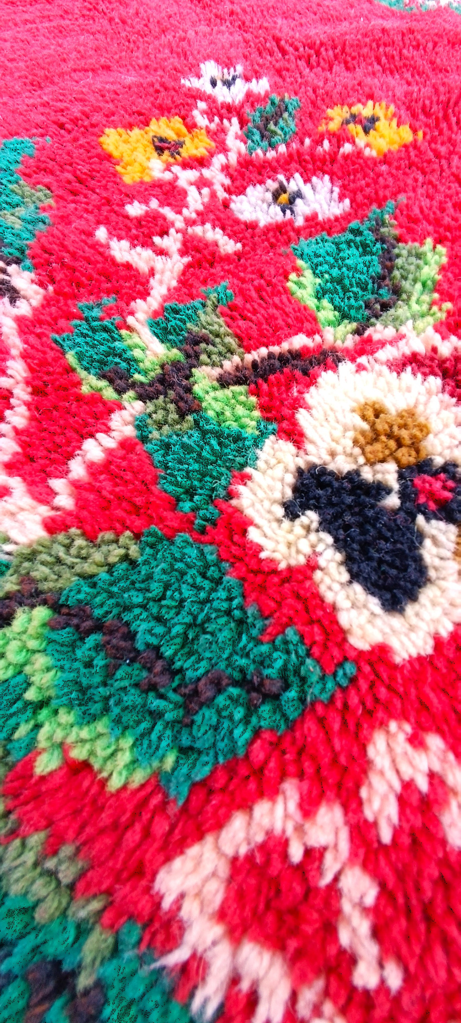 Close-up detail of a vintage Bulgarian handwoven wool kitenik with dense red pile, green leaves and multicoloured floral motifs