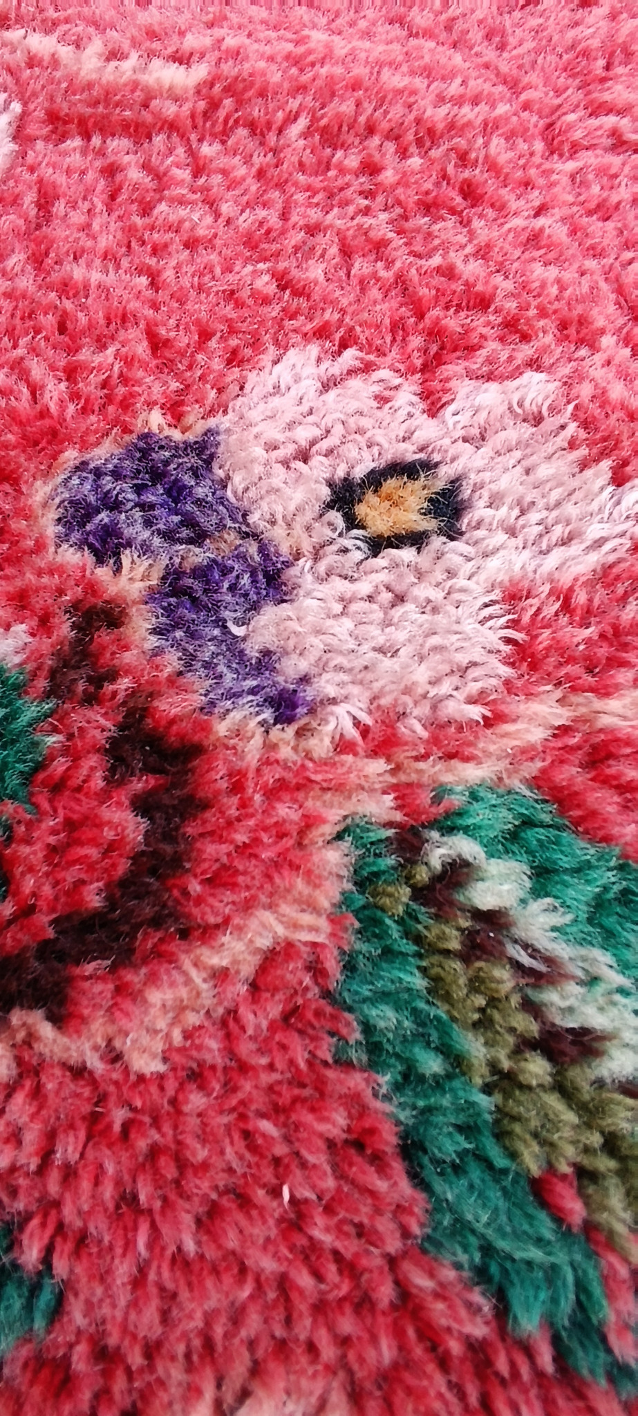 Close-up of a vintage Bulgarian handwoven wool kitenik showing dense red pile, cream and purple flowers, green leaves and natural wool texture