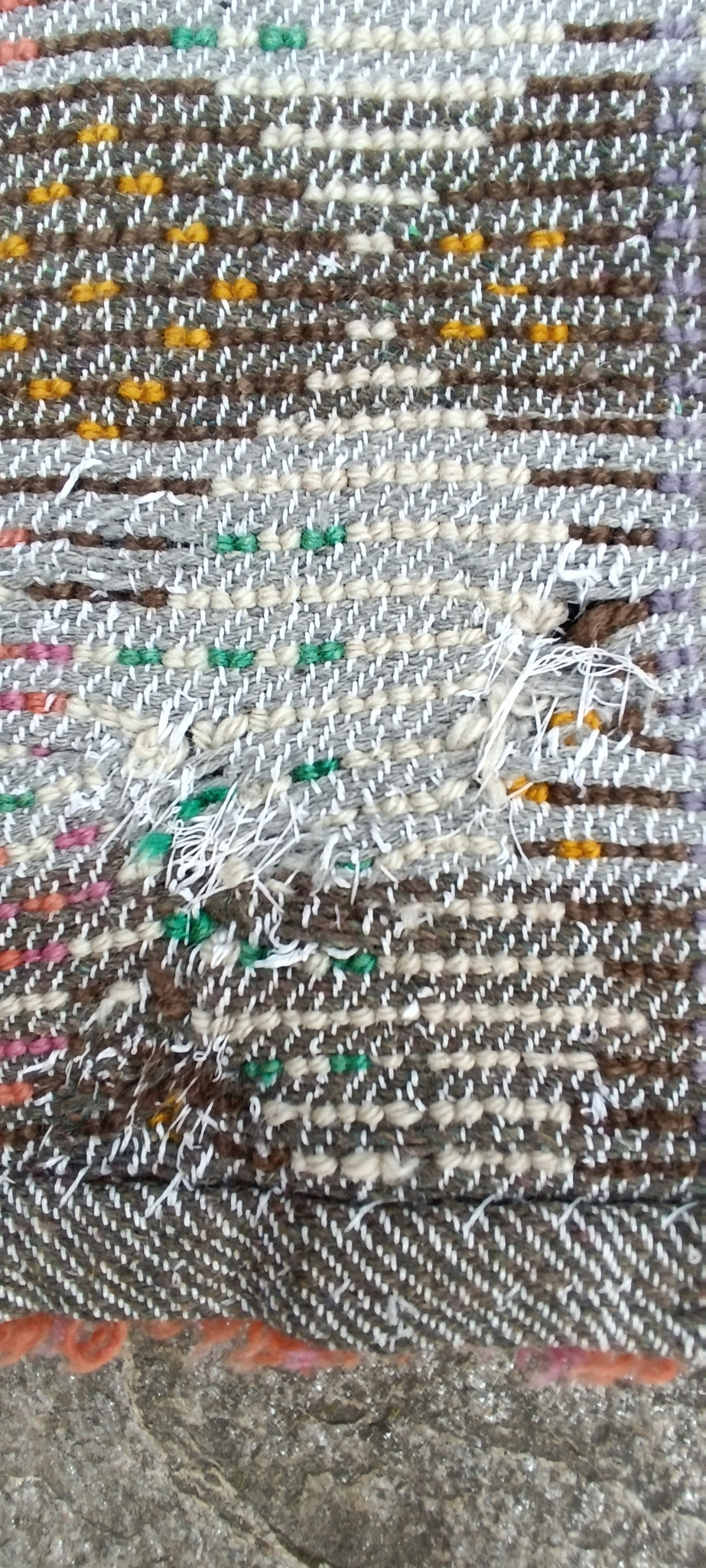 Close-up of the reverse side of a vintage Bulgarian wool kitenik showing the woven foundation and a small repaired area with visible threads