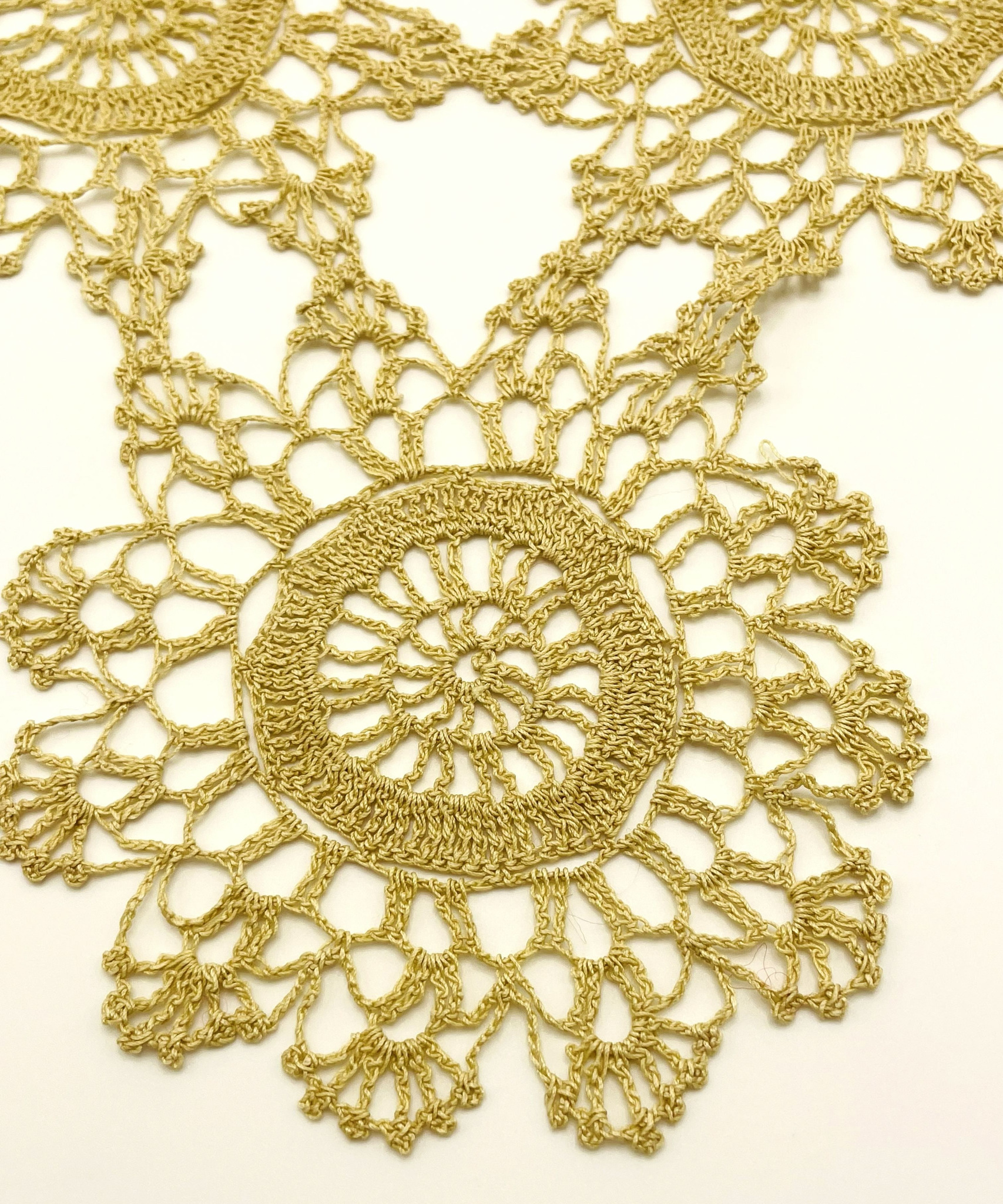 Close-up of a vintage handmade gold-tone crochet doily showing an openwork rosette motif and fine hand-crocheted details