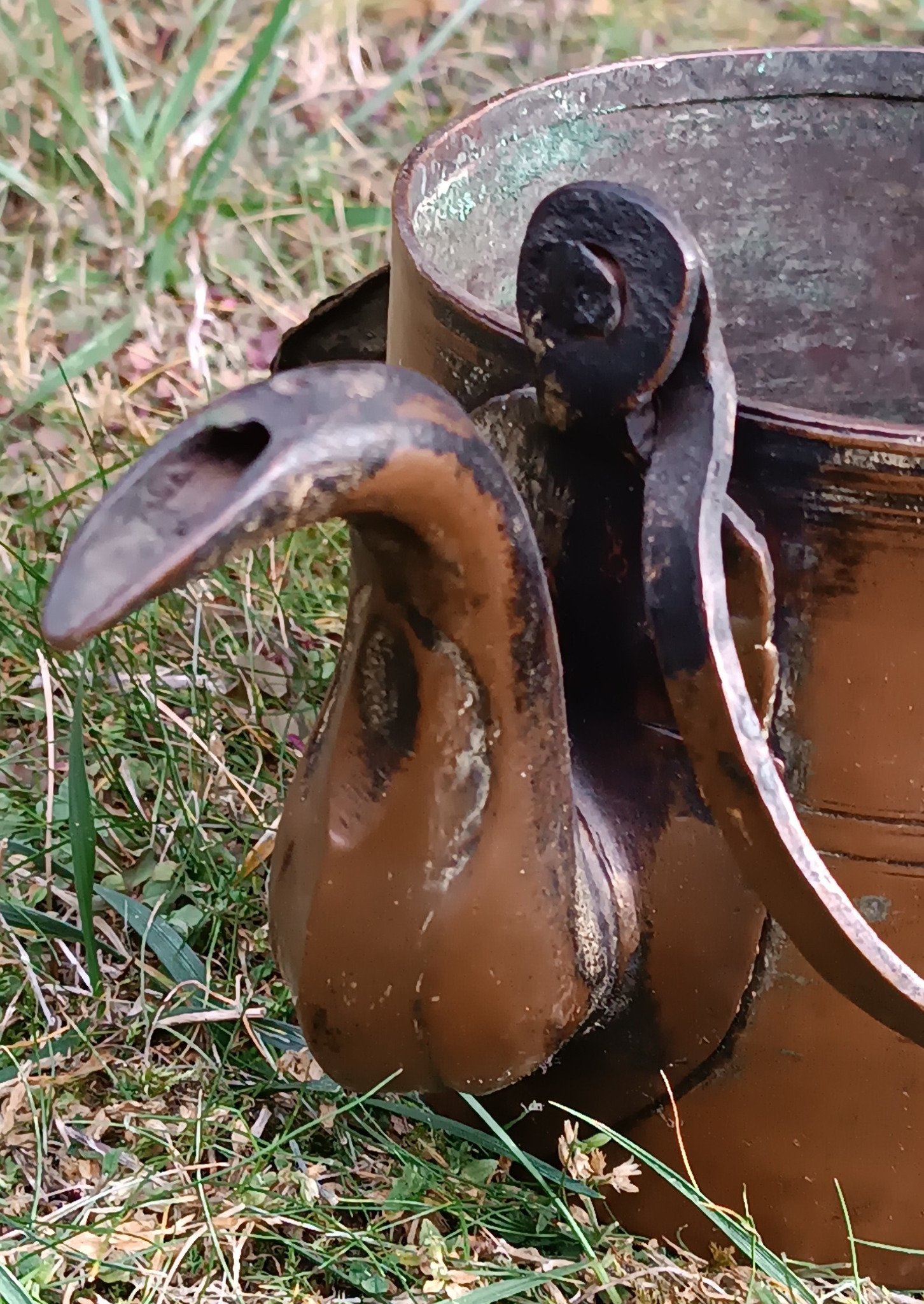 Close-up of antique copper kettle gooseneck spout opening, riveted handle fittings and aged iron carrying handle