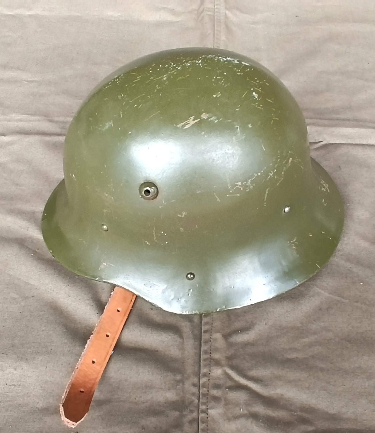 Bulgarian M36 Type A steel helmet refurbished for the Bulgarian People's Army, showing its rounded crown, olive-green shell, ventilation hole, rivets and leather chinstrap.