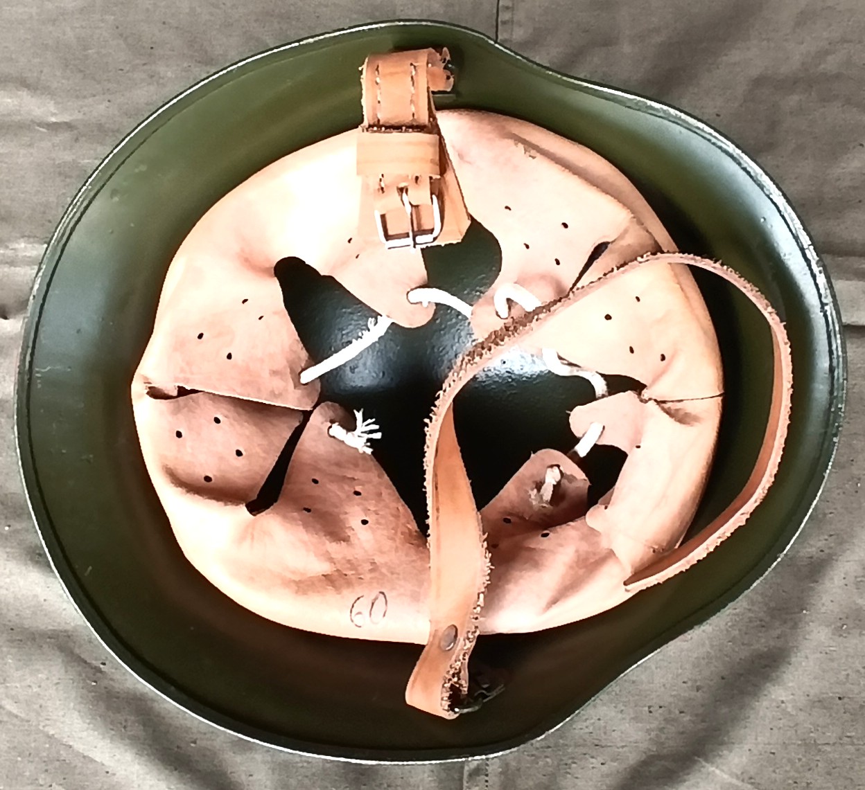 Interior of a Bulgarian M36 Type A helmet showing the tan leather liner, white adjustment cord, chinstrap buckle and handwritten number 60.