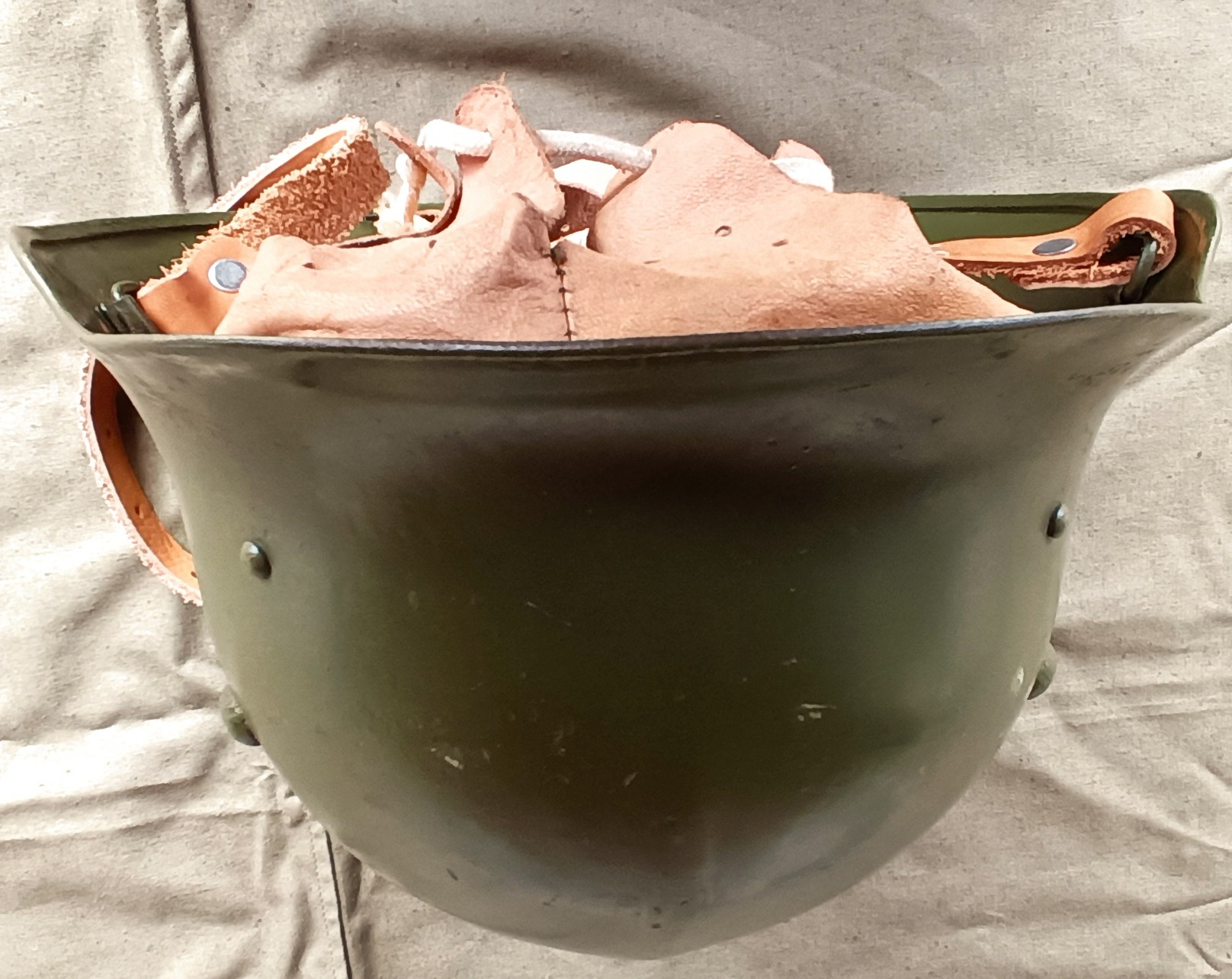 Bulgarian M36 Type A steel helmet with visible leather liner, retaining rivets and olive-green shell, photographed upside down to document its BNA refurbishment.