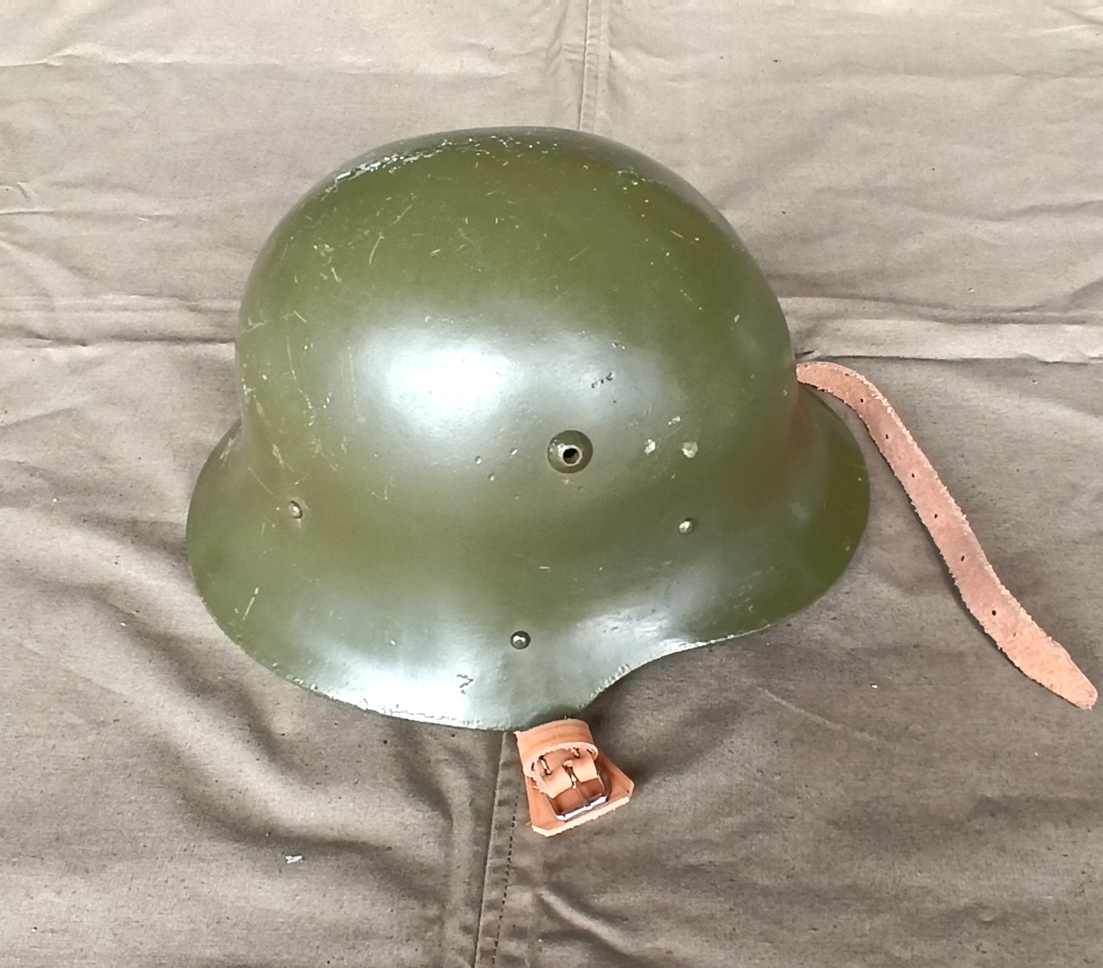 Bulgarian M36 Type A steel helmet with olive-green shell, ventilation opening, retaining rivets and leather chinstrap with buckle, refurbished for the BNA.