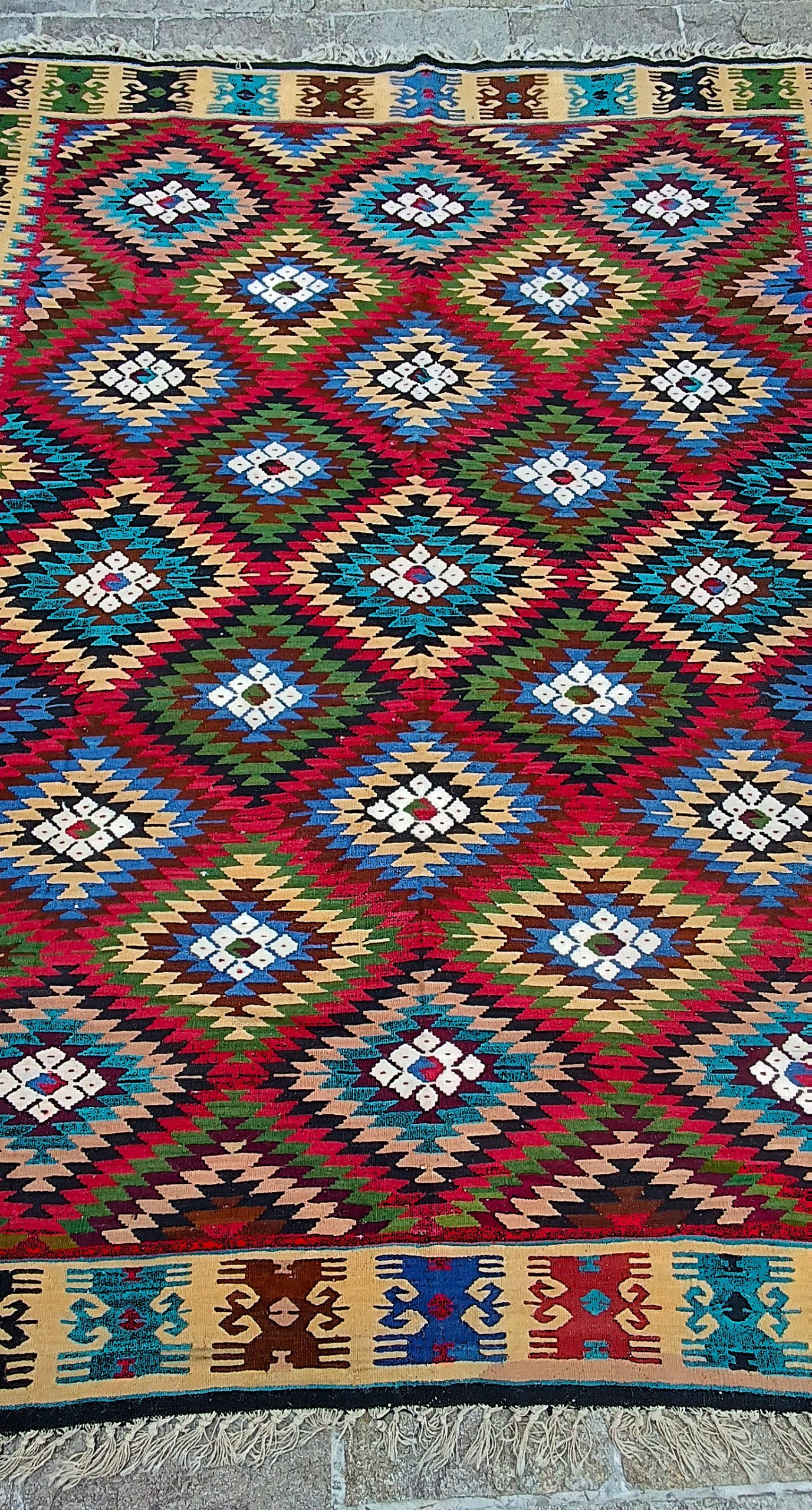 Central field of a Bakamski with Sofra rug showing symmetrical multicoloured diamonds and patterned cream borders at both ends.