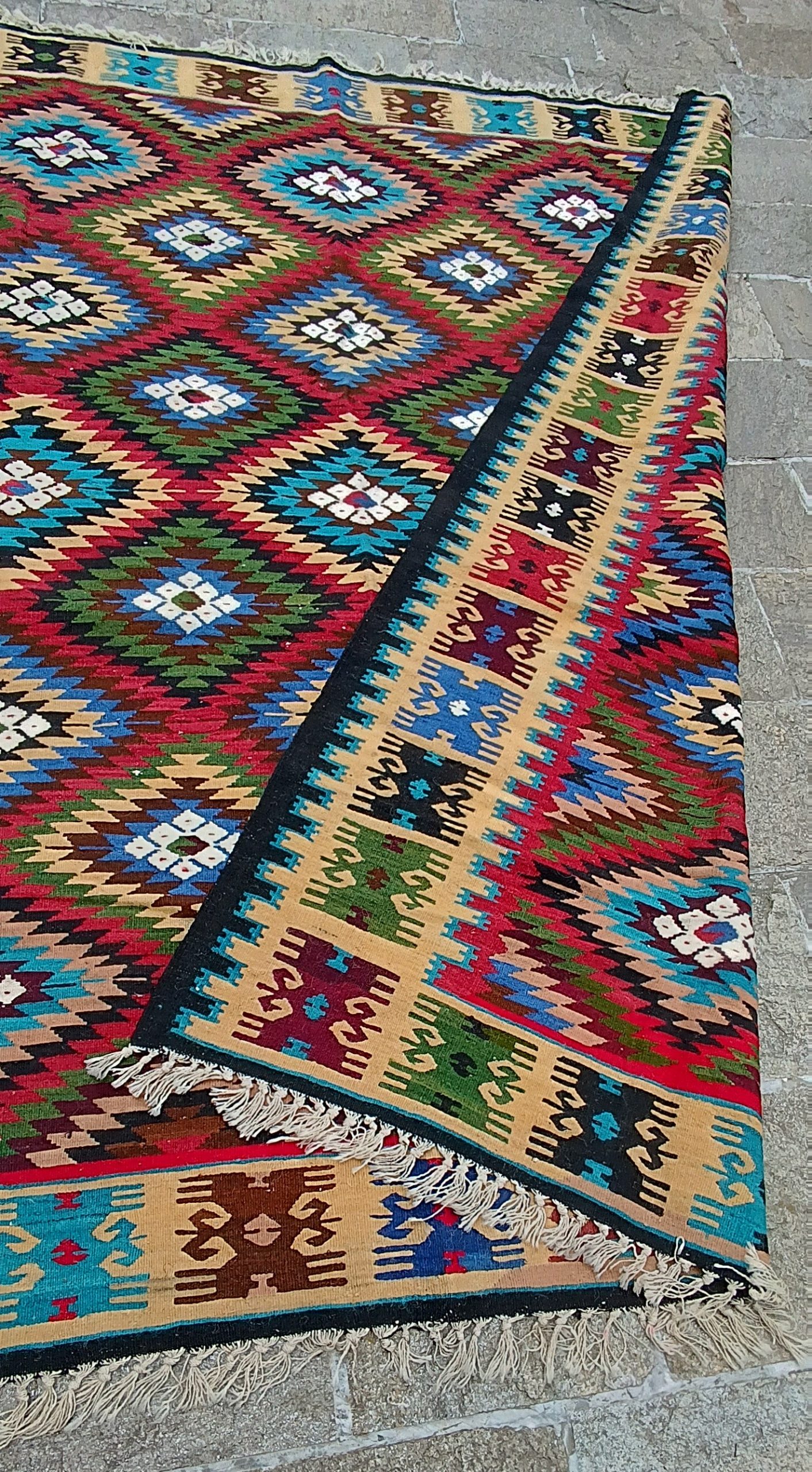 Folded corner of a Bakamski with Sofra wool kilim showing reversible patterns, decorated border and white hand-knotted fringes.