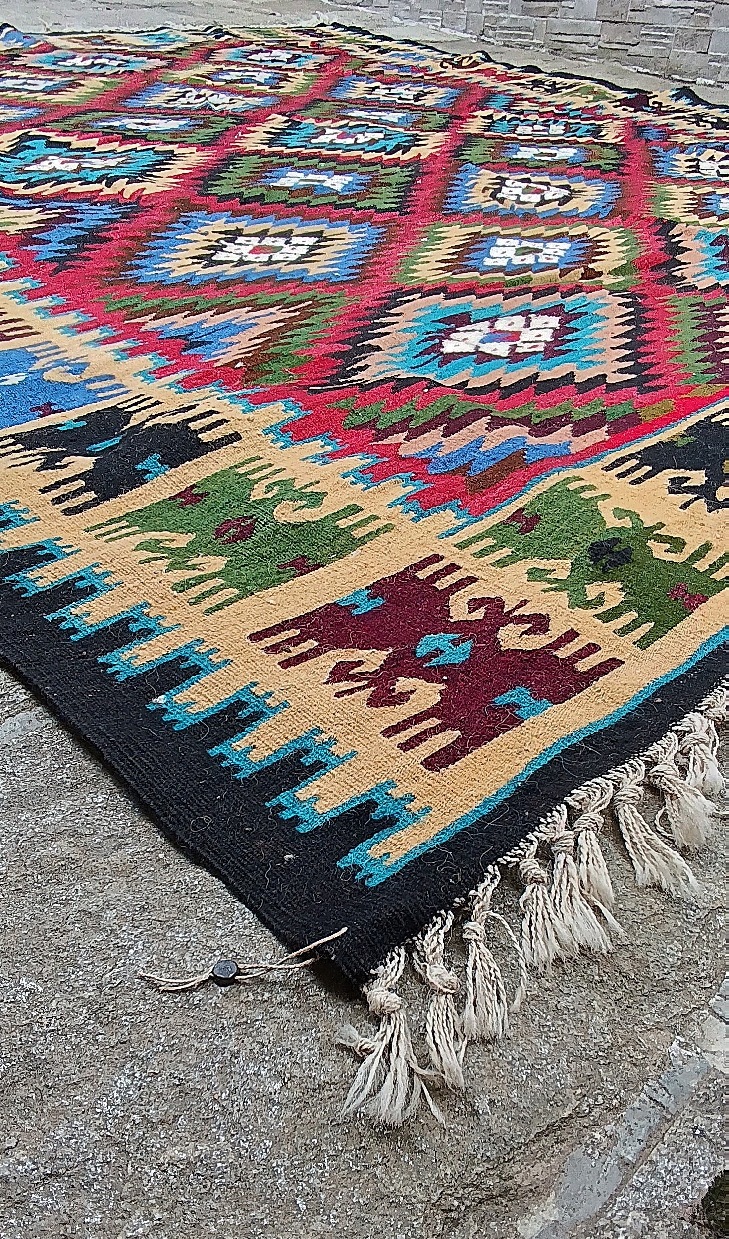 Low-angle view of the Bakamski rug with diamond medallions, cream border, white fringes and an attached seal at the corner.