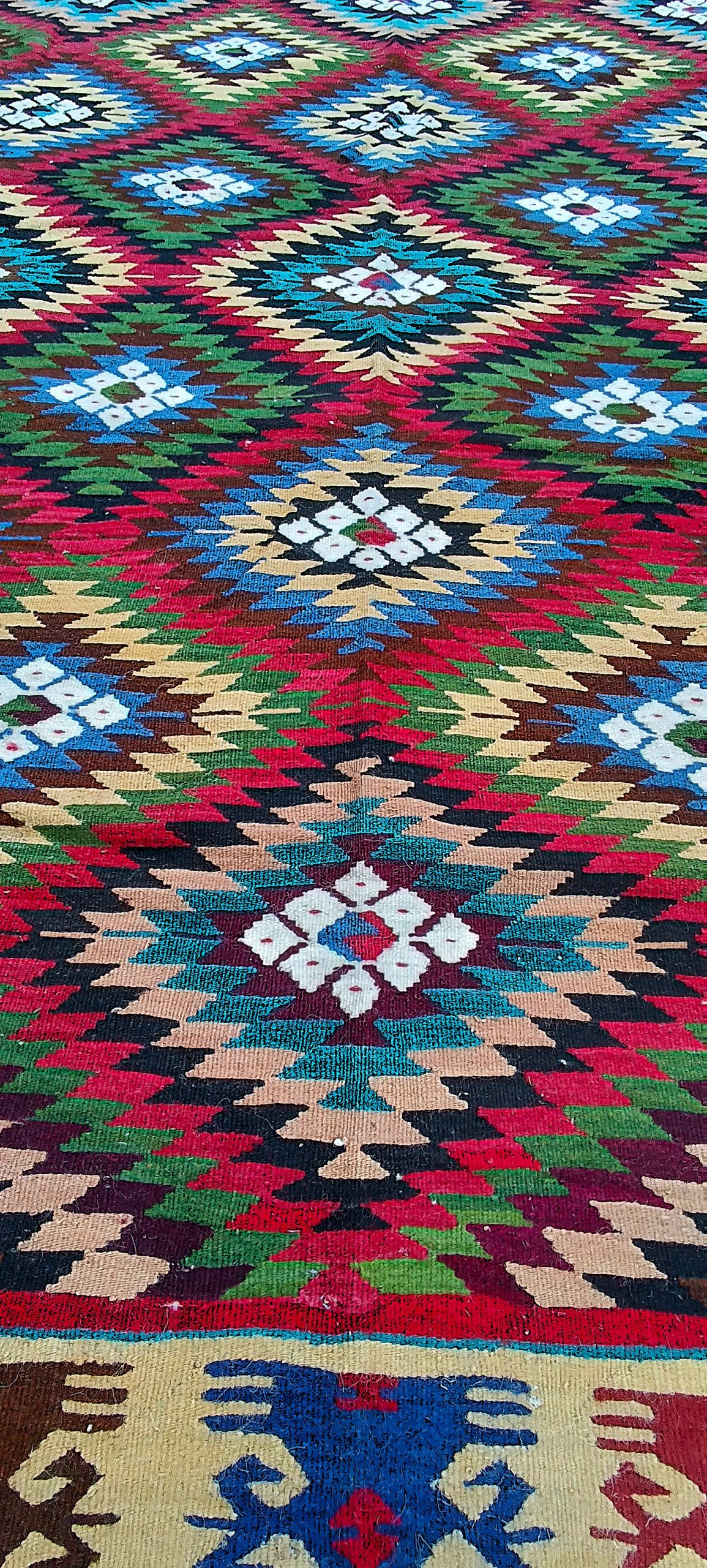 Perspective along the woven field of a Bakamski rug showing diagonal rows of stepped diamonds and white Sofra flowers.