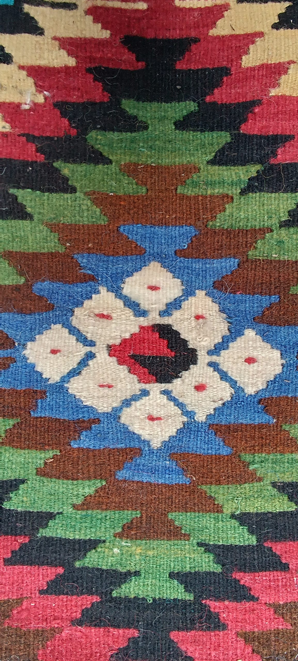 Eight-part white Sofra rosette with red accents inside a blue geometric field, surrounded by green, brown and crimson wool patterns.