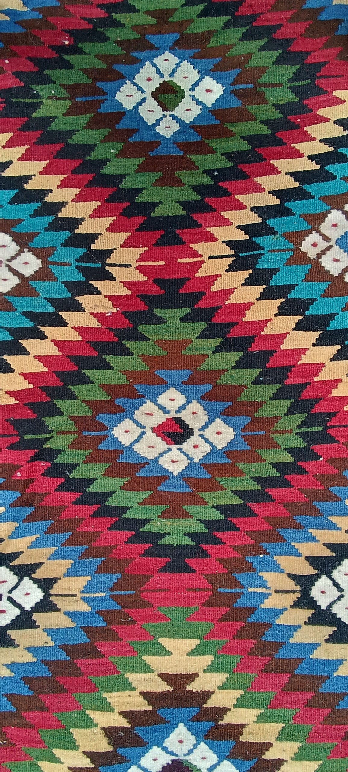 Close-up of white Sofra geometric rosettes surrounded by crimson, blue, green and ochre stepped diamonds in a Chiprovtsi rug.