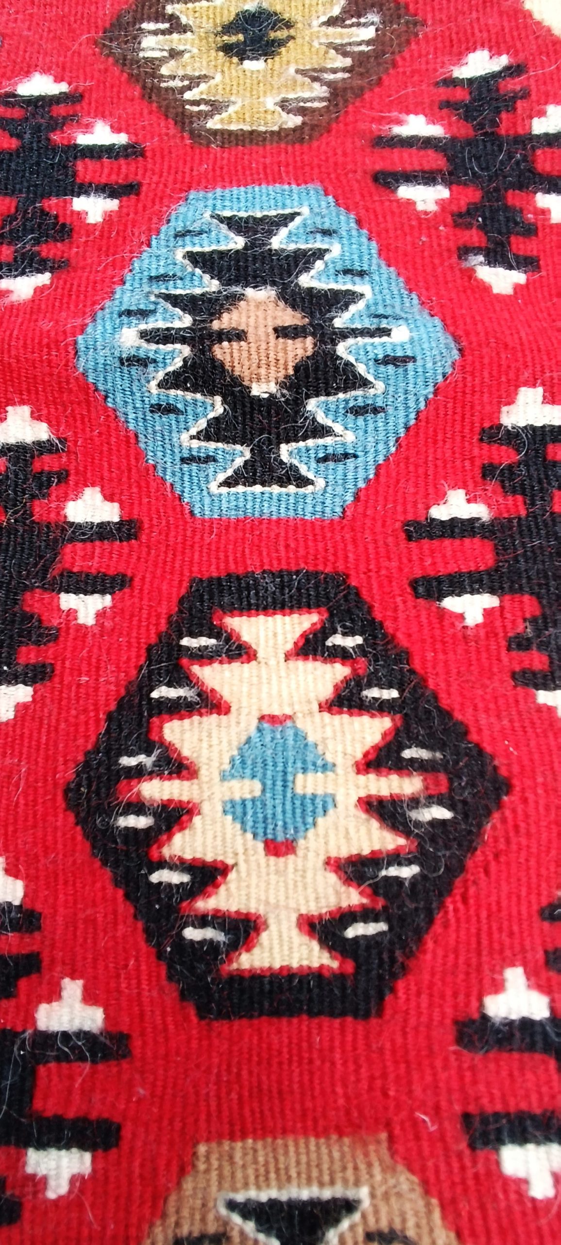 Macro detail of blue and black stepped diamond motifs with cream highlights on a vivid red Chiprovtsi Bombichki rug.