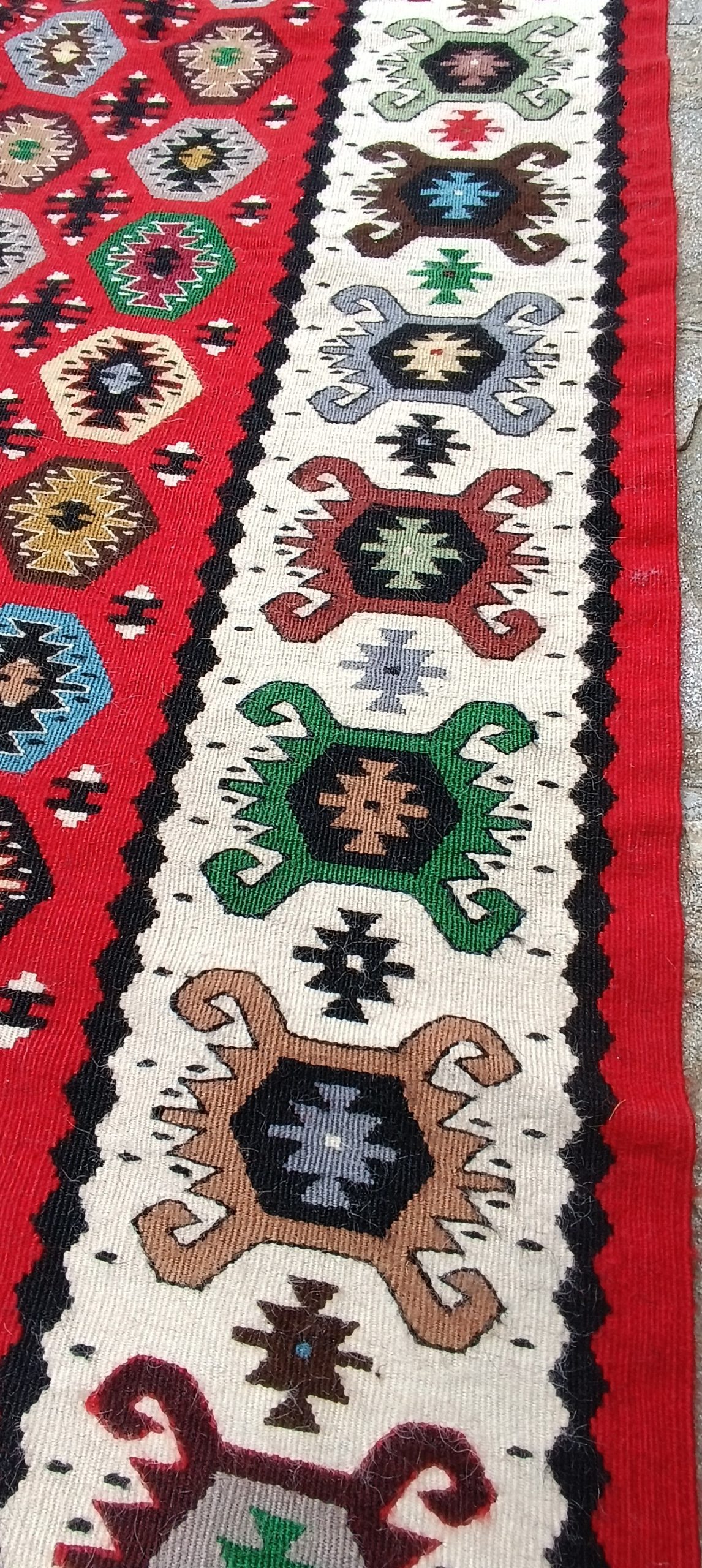 Close-up of the cream border of a Chiprovtsi Bombichki rug with blue, green and brown angular ornaments next to a red geometric field.