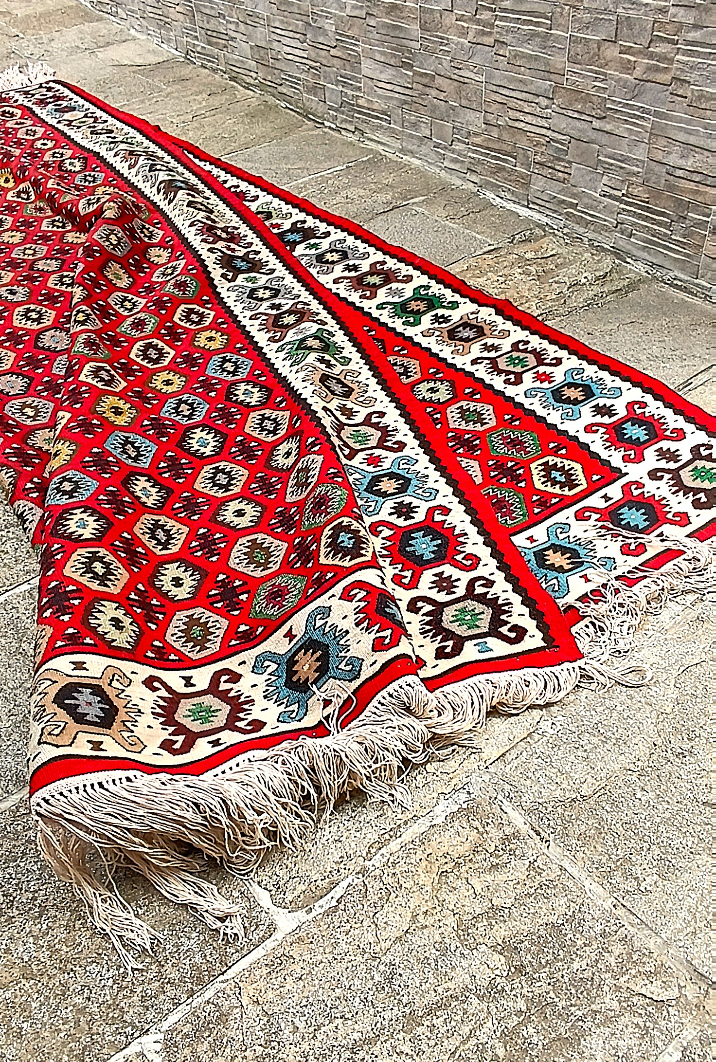 Folded corner of the Chiprovtsi Bombichki kilim showing geometric patterning on both sides, the cream border and white fringes.