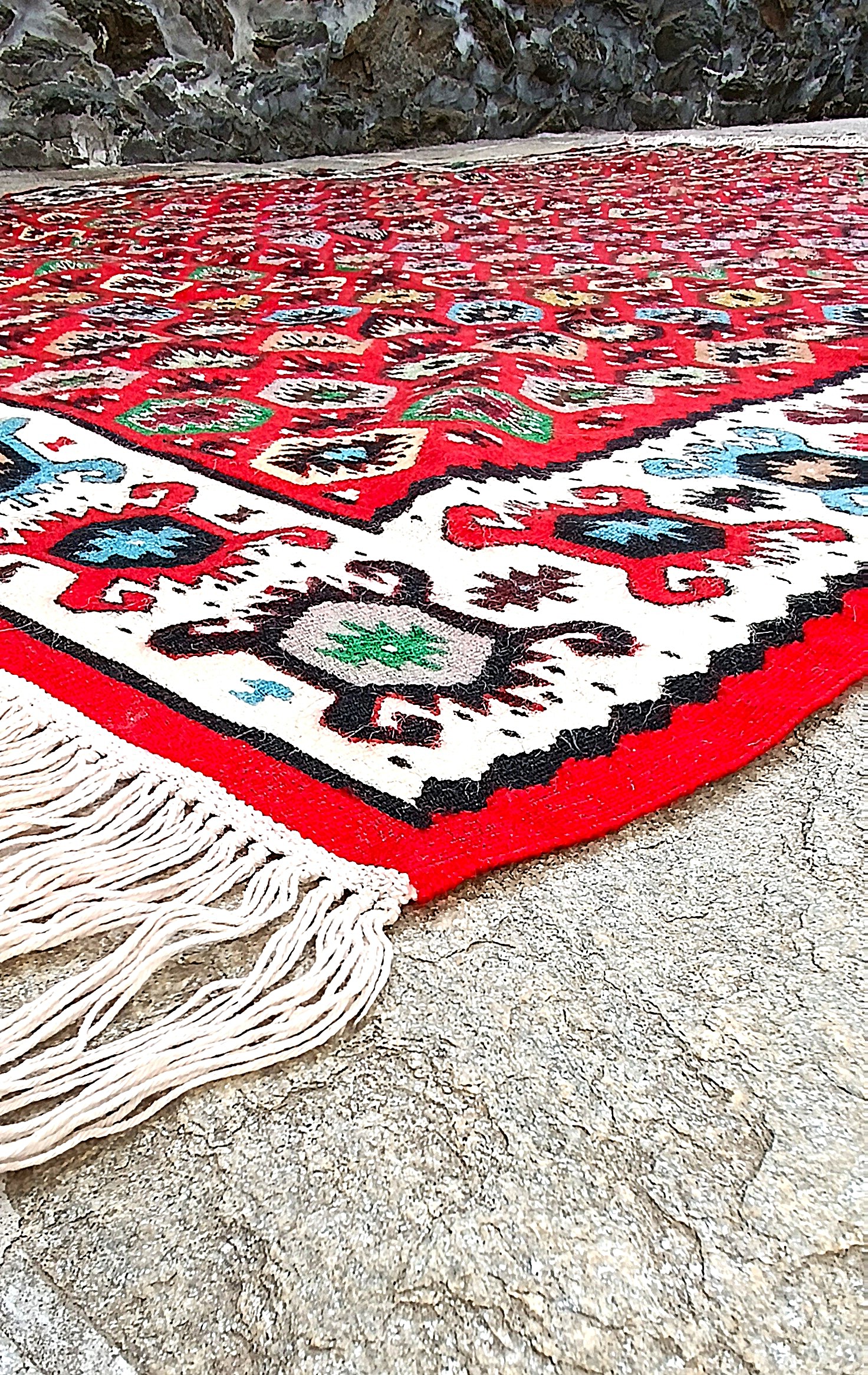 Low-angle view across the red Bombichki rug, showing its flatwoven surface, cream border and white warp fringes.