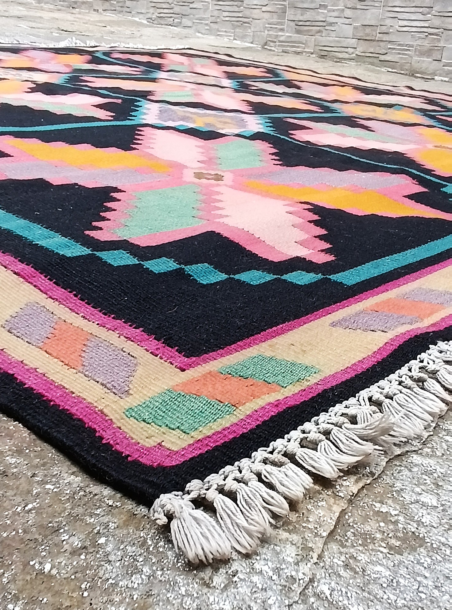 Close-up of the corner of the Christmas Star Chiprovtsi rug with a pastel geometric border, pink stars and white fringes.