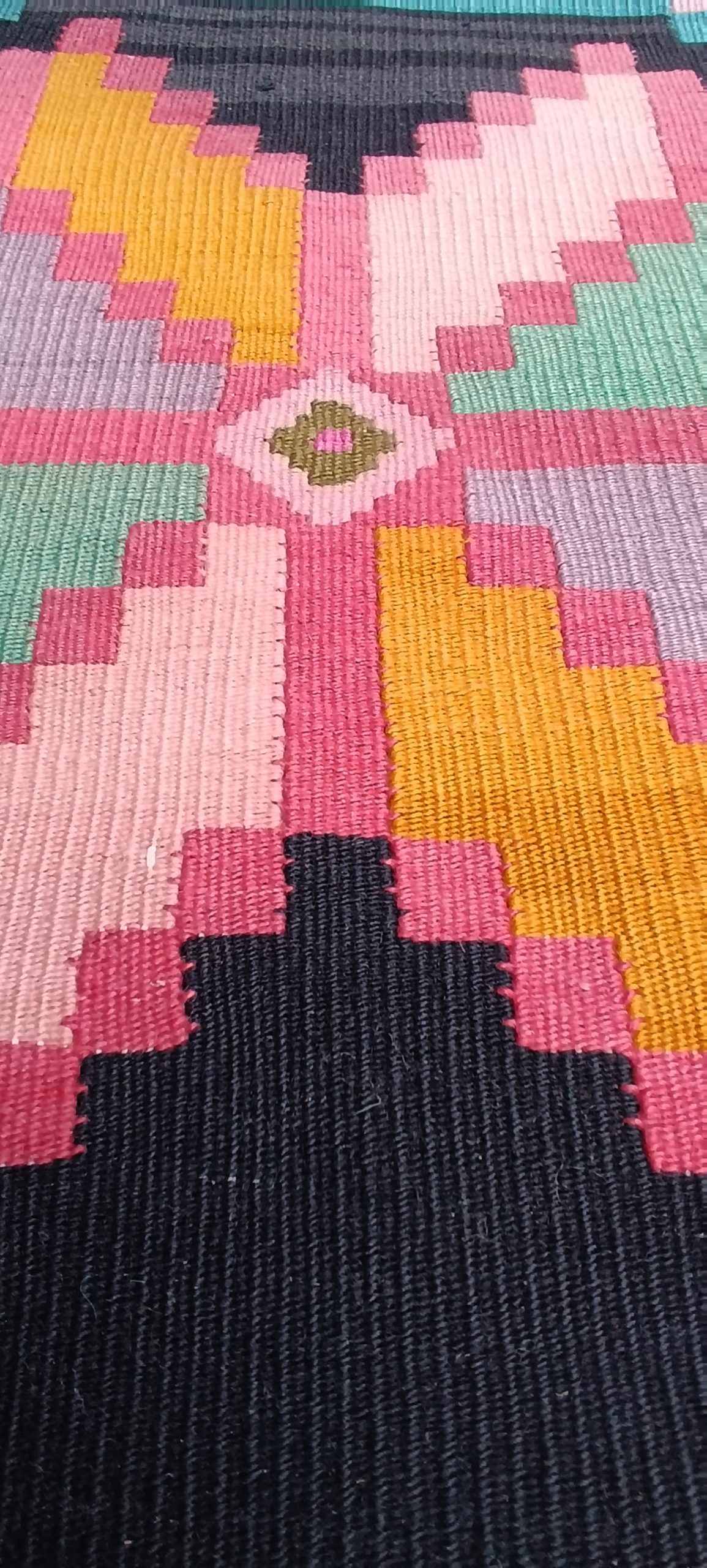 Macro photograph of an eight-pointed pink, green, lavender and golden-yellow star with a small central diamond on a handwoven Chiprovtsi rug.