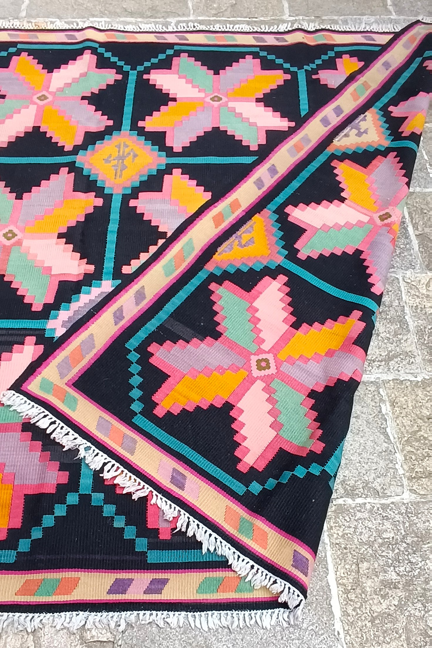 Folded corner of the Christmas Star Chiprovtsi rug revealing reversible weaving, star ornaments, patterned border and white fringes.