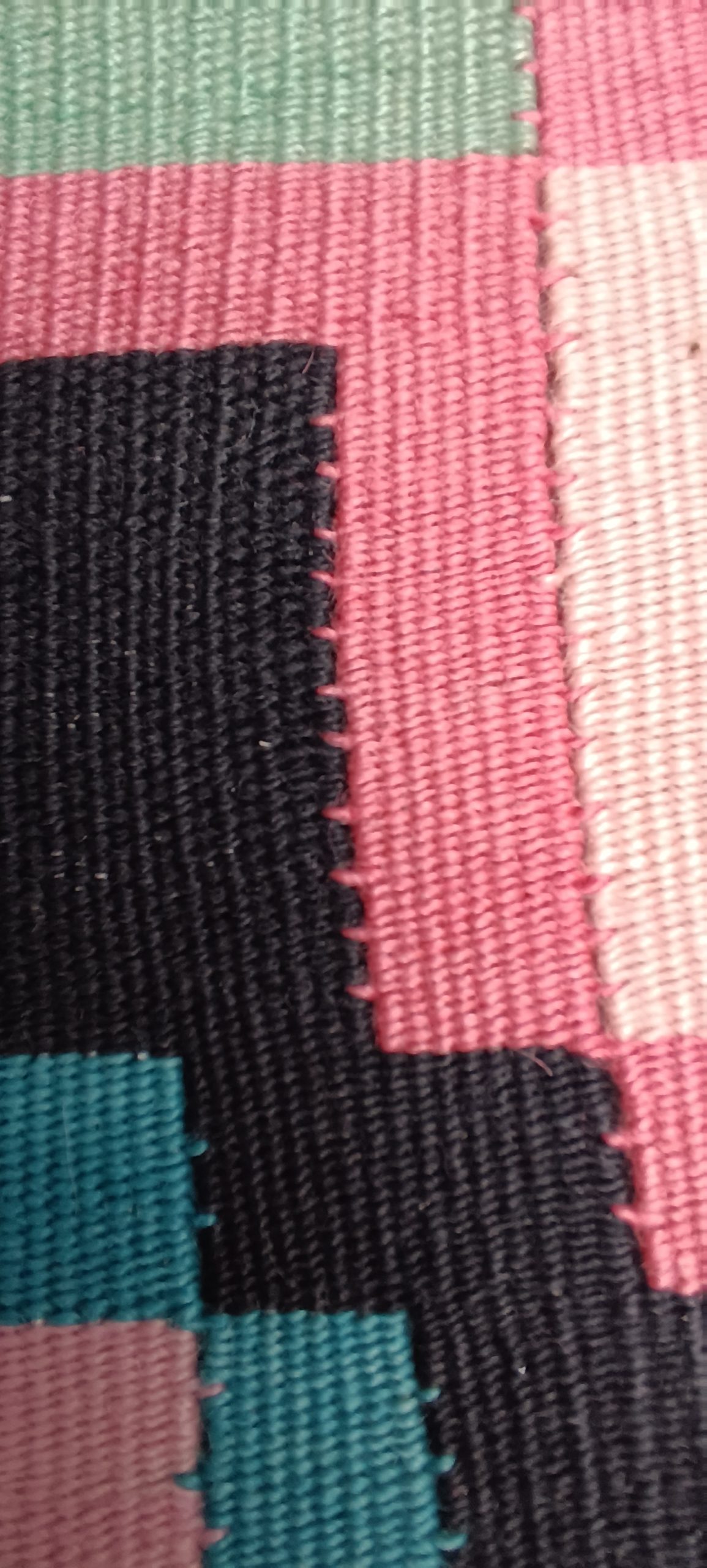 Extreme macro detail of a handwoven Chiprovtsi rug showing pink, mint-green, cream and black threads and stepped colour transitions.