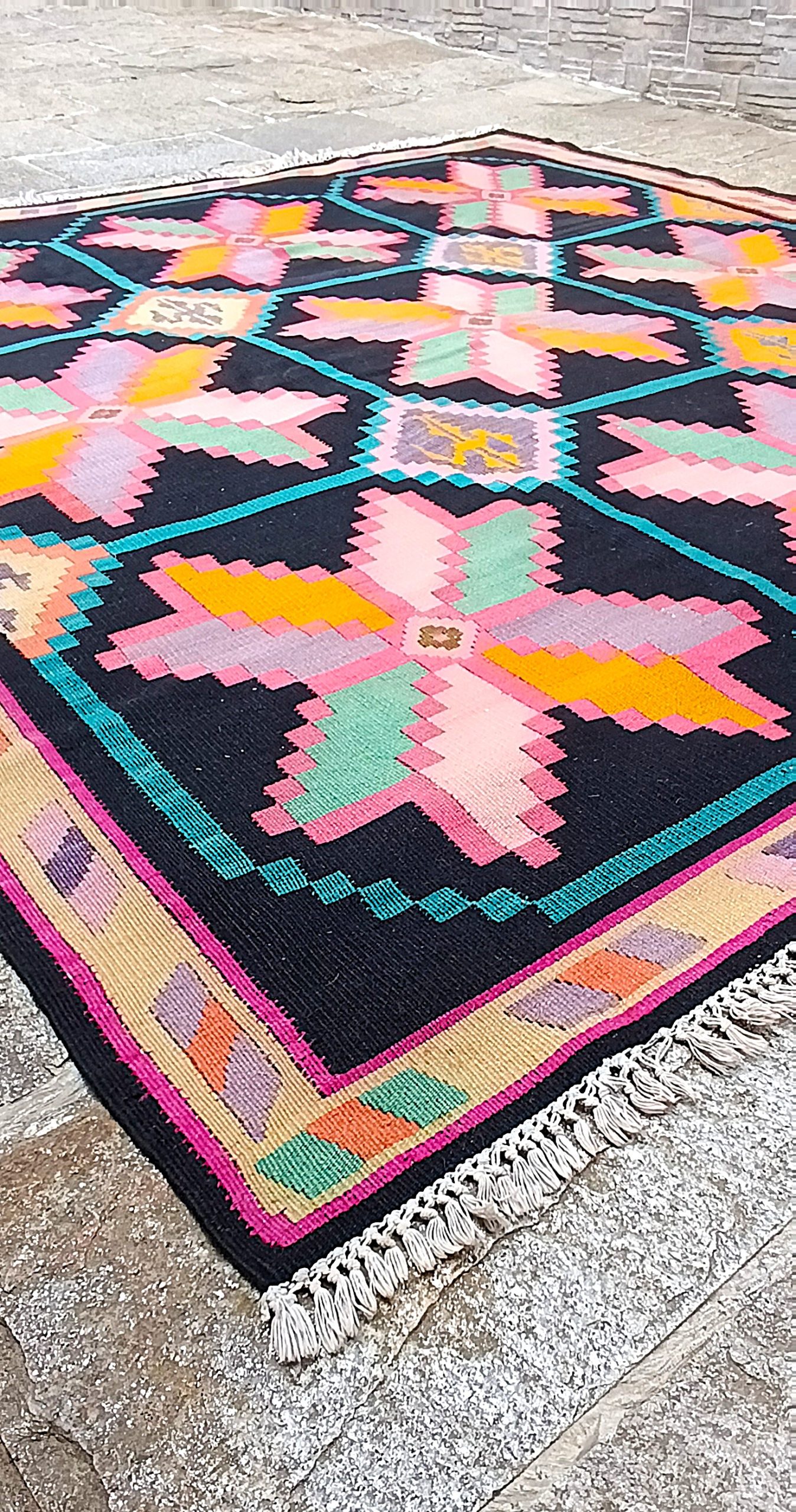 Low-angle photograph of a Bulgarian Chiprovtsi rug with pink geometric stars, turquoise lines, patterned border and white fringes.