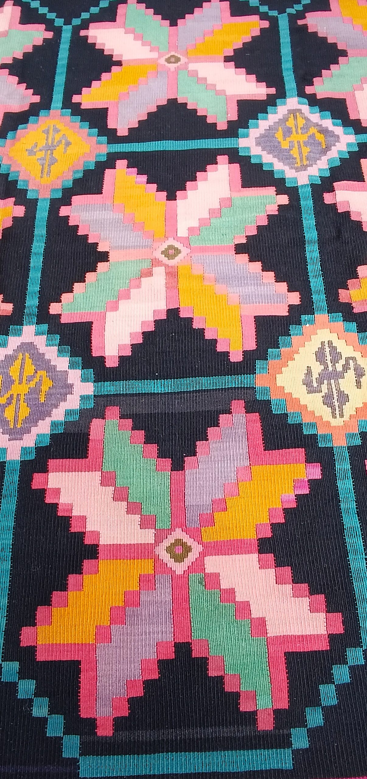 Close-up of multicoloured star motifs and diamond-shaped medallions connected by turquoise lines on a black Chiprovtsi rug.