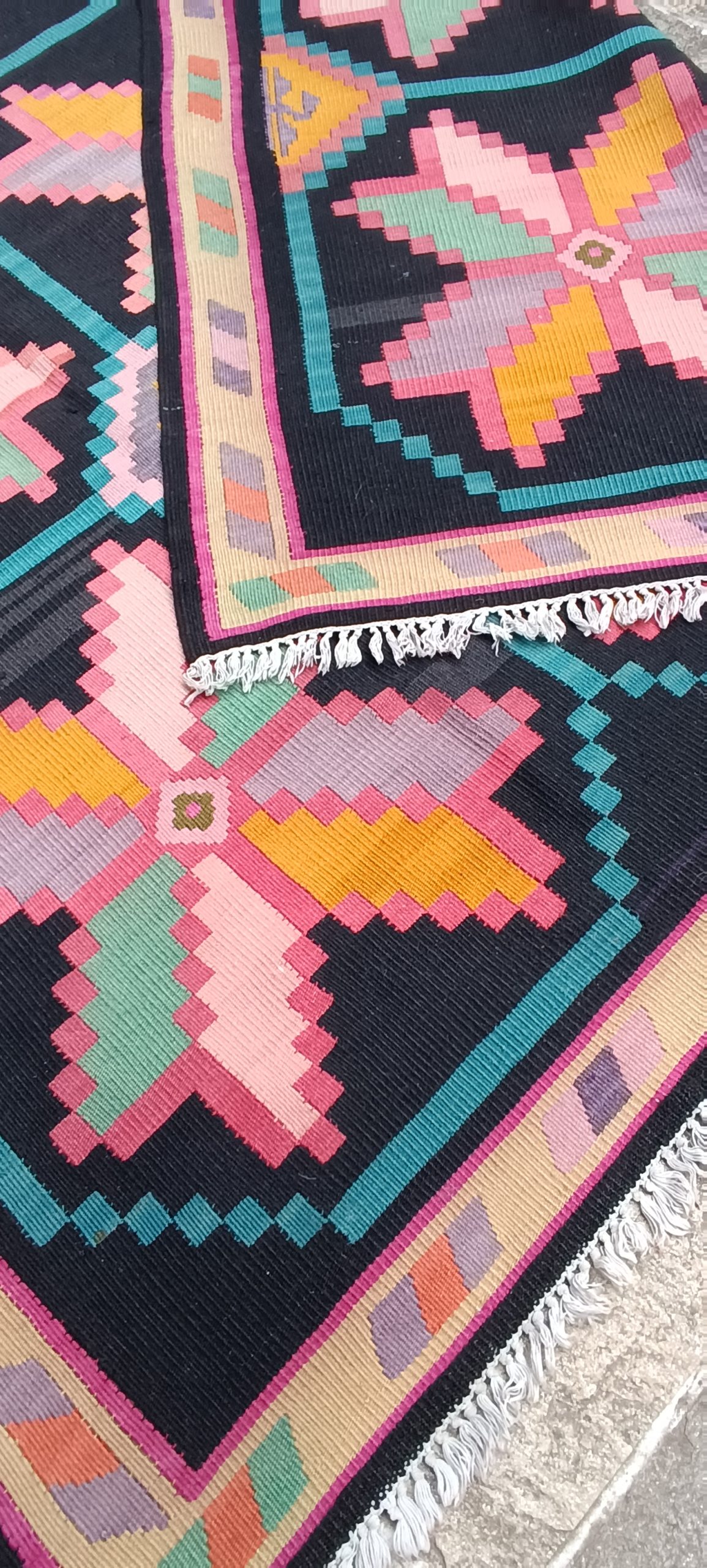Detail of a folded reversible Bulgarian Chiprovtsi rug with large pastel stars, turquoise lines and white fringe finishing.
