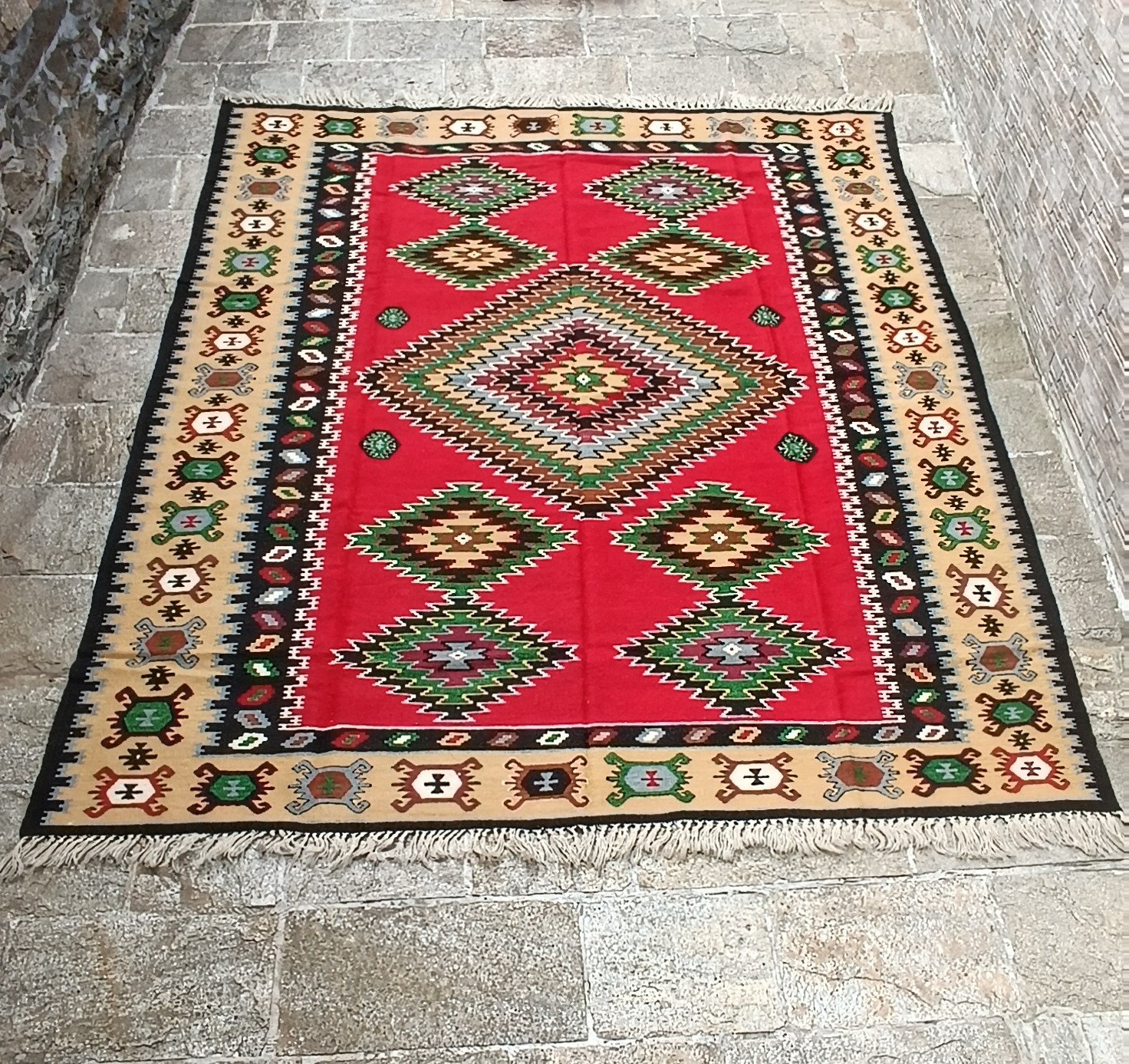 Traditional red rug with a large central stepped diamond, symmetrical multicoloured geometric motifs, a cream ornamental border and white fringes.