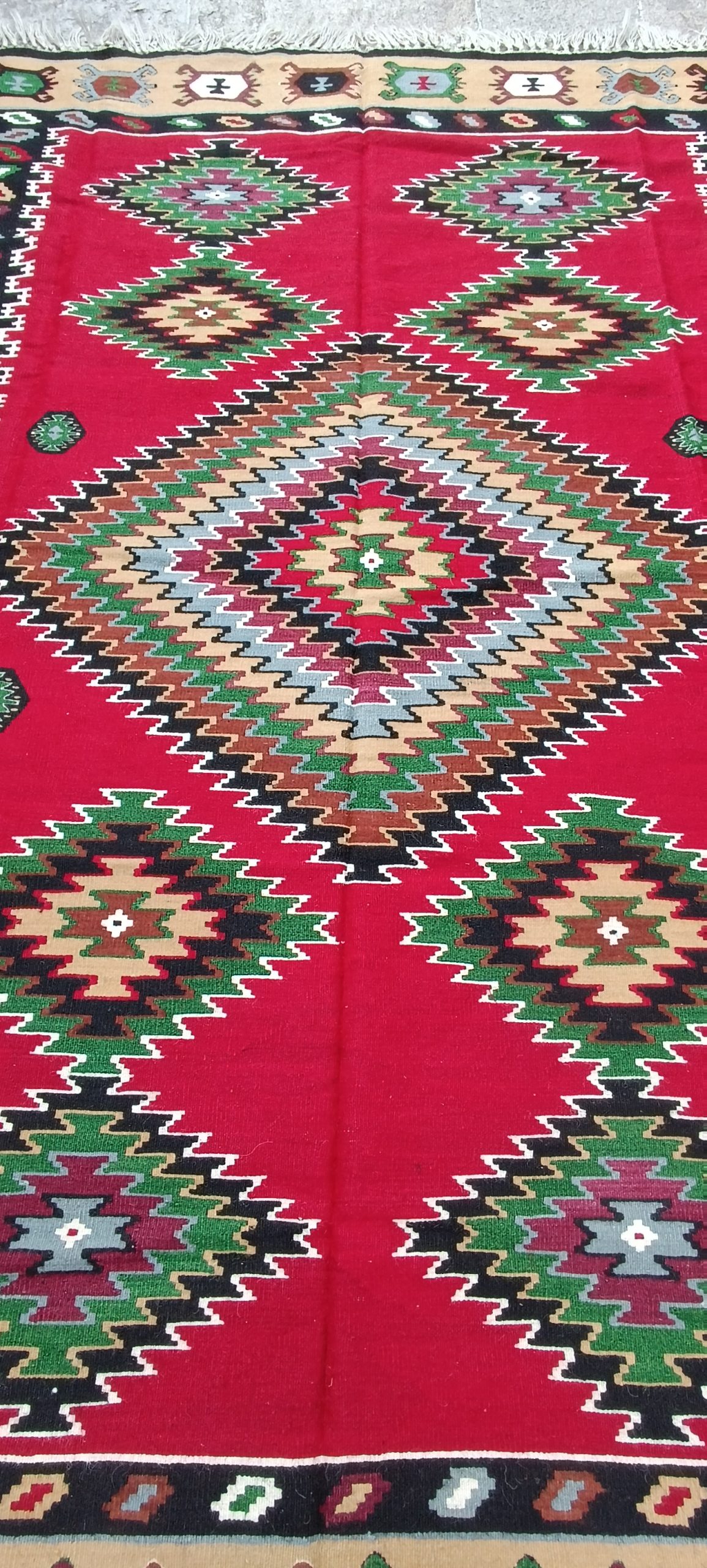 Central geometric composition of an old Bulgarian Chiprovtsi rug with a large multicoloured stepped diamond and symmetrical motifs on a vivid red background.