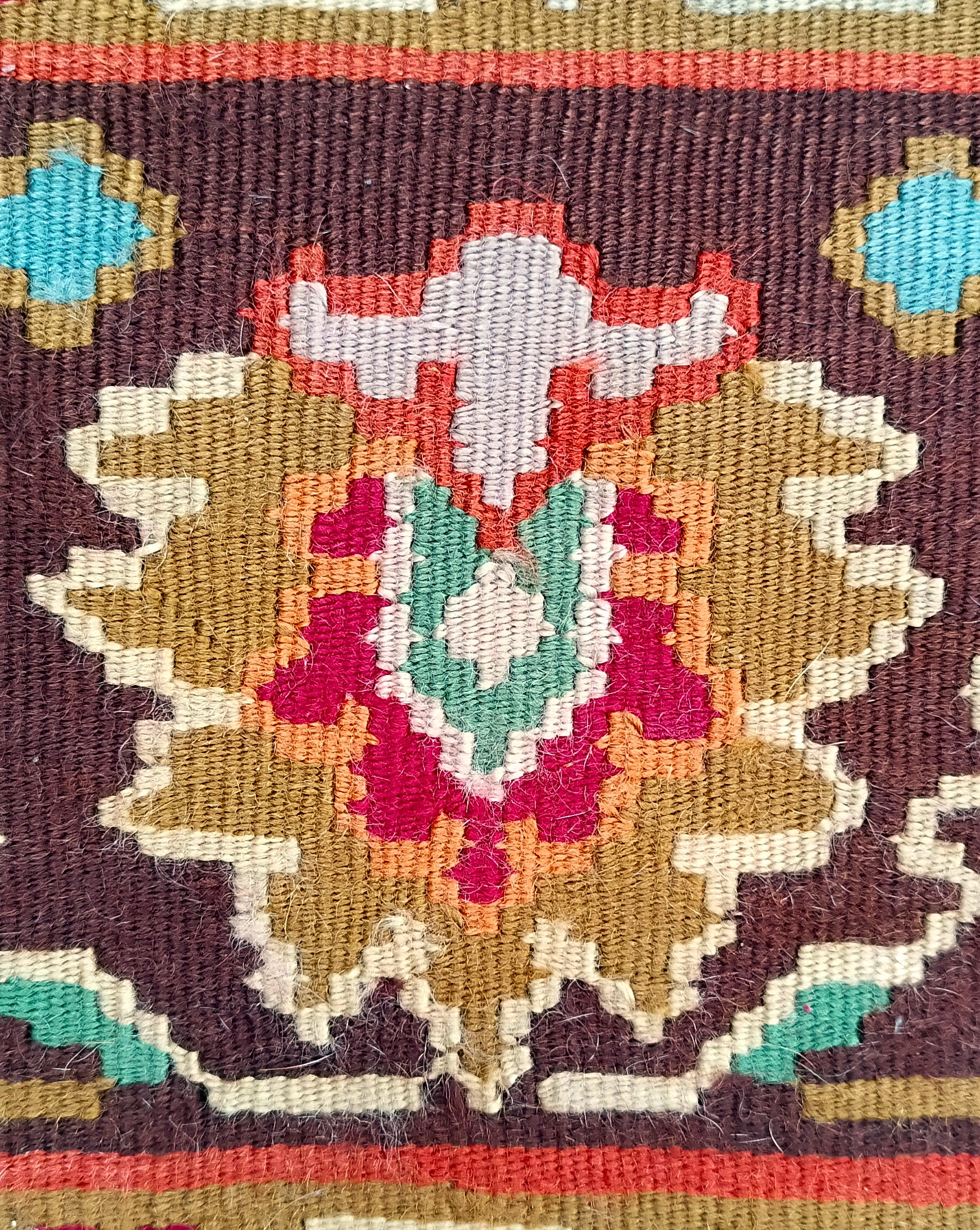 Detailed multicoloured flower woven into the dark brown border of a traditional Bulgarian Kotel rug