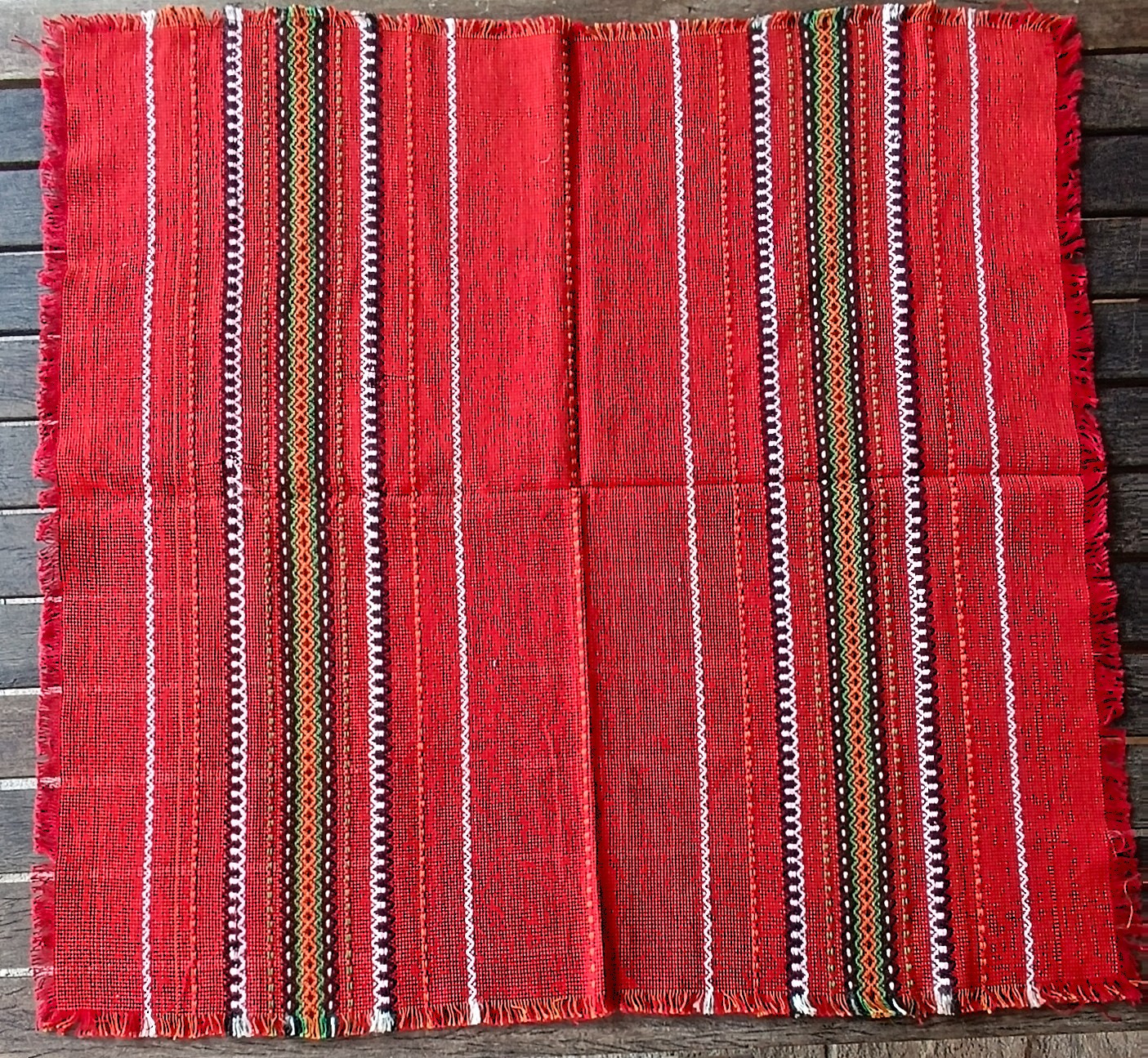 Vintage Bulgarian folk tablecloth with red woven ground, geometric striped decoration and fringed edges, approximately 79 × 75 cm