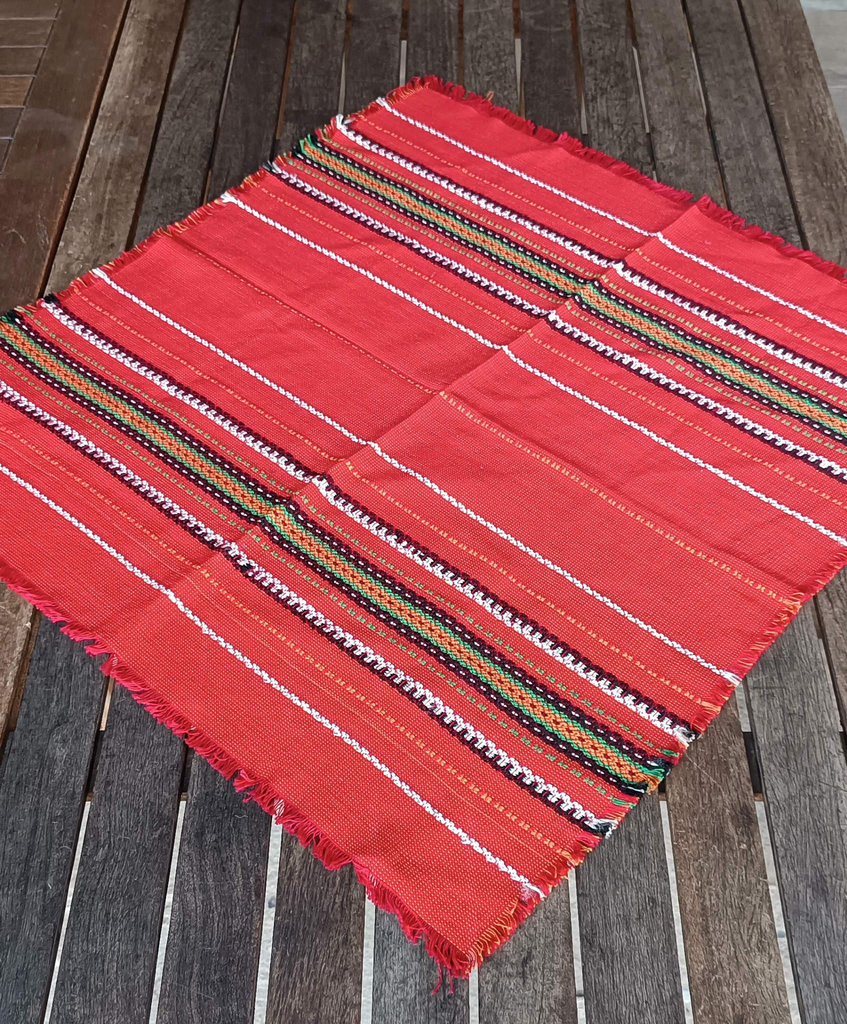 Vintage Bulgarian folk tablecloth with red woven ground, traditional geometric stripes and fringed edges, shown at an angle